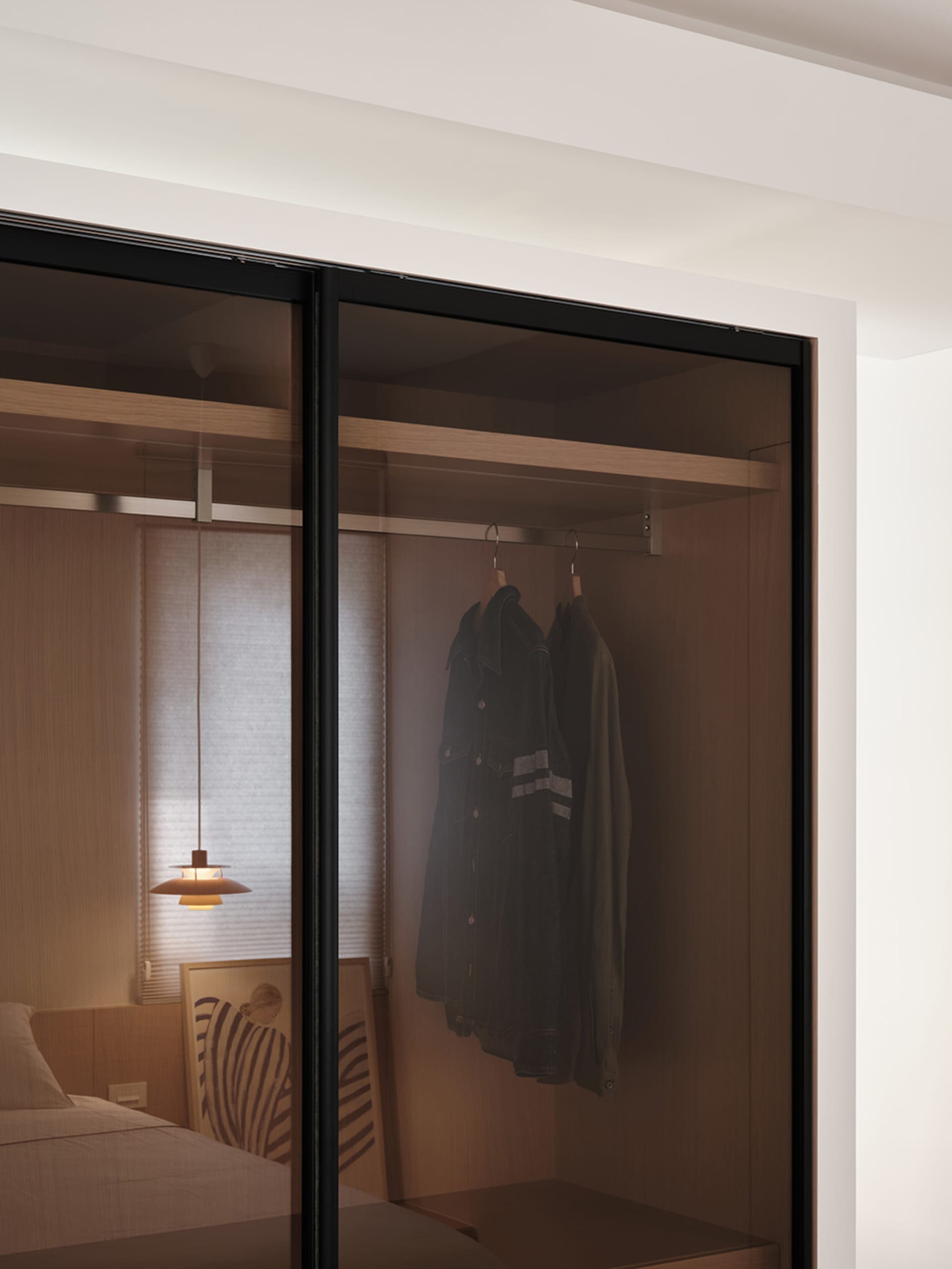 Minimalist closet with glass doors and wooden interiors, featuring casual attire hanging on a rail.