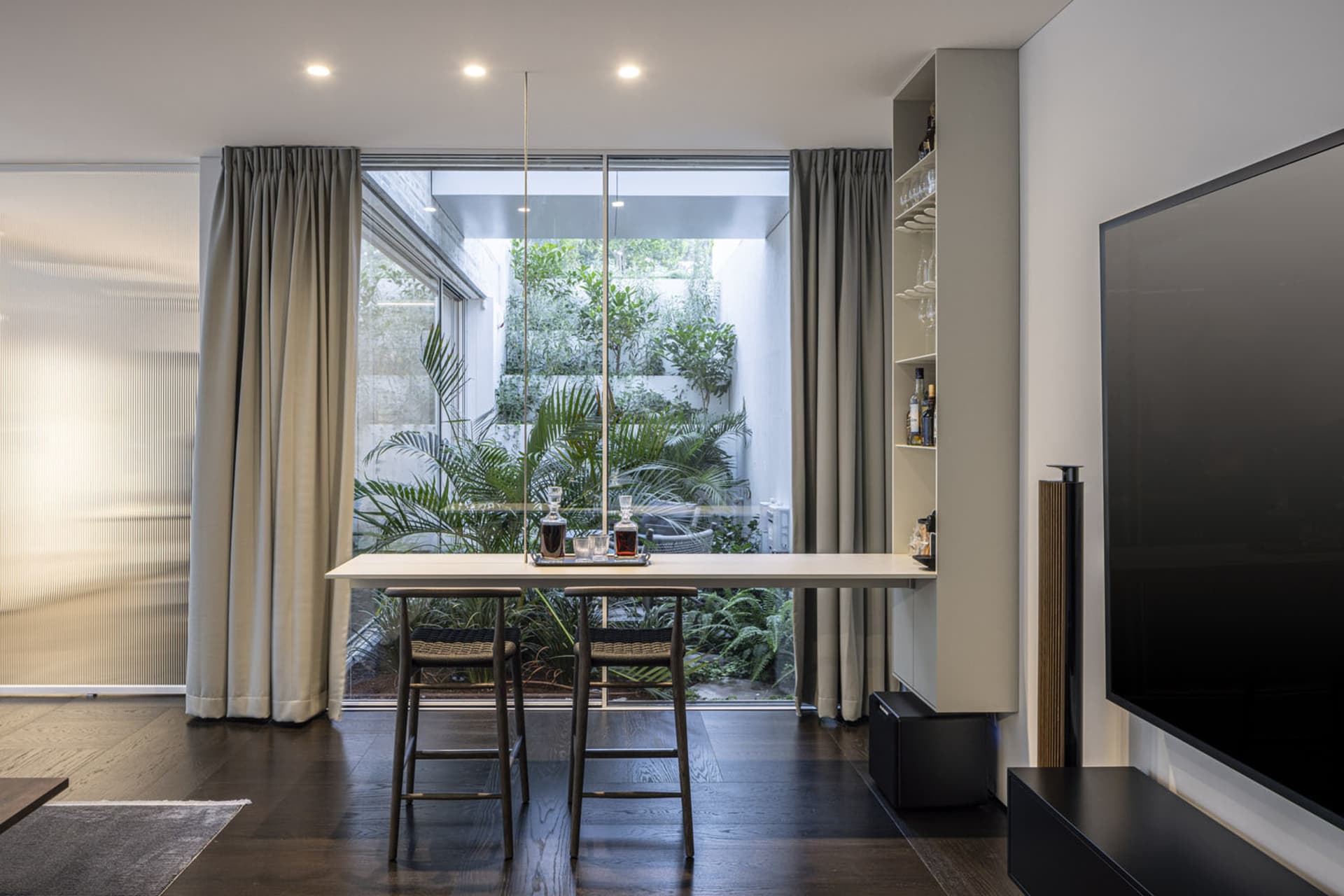 A modern living room featuring a high-end interior design with wooden floors, glass walls, and a mix of materials.