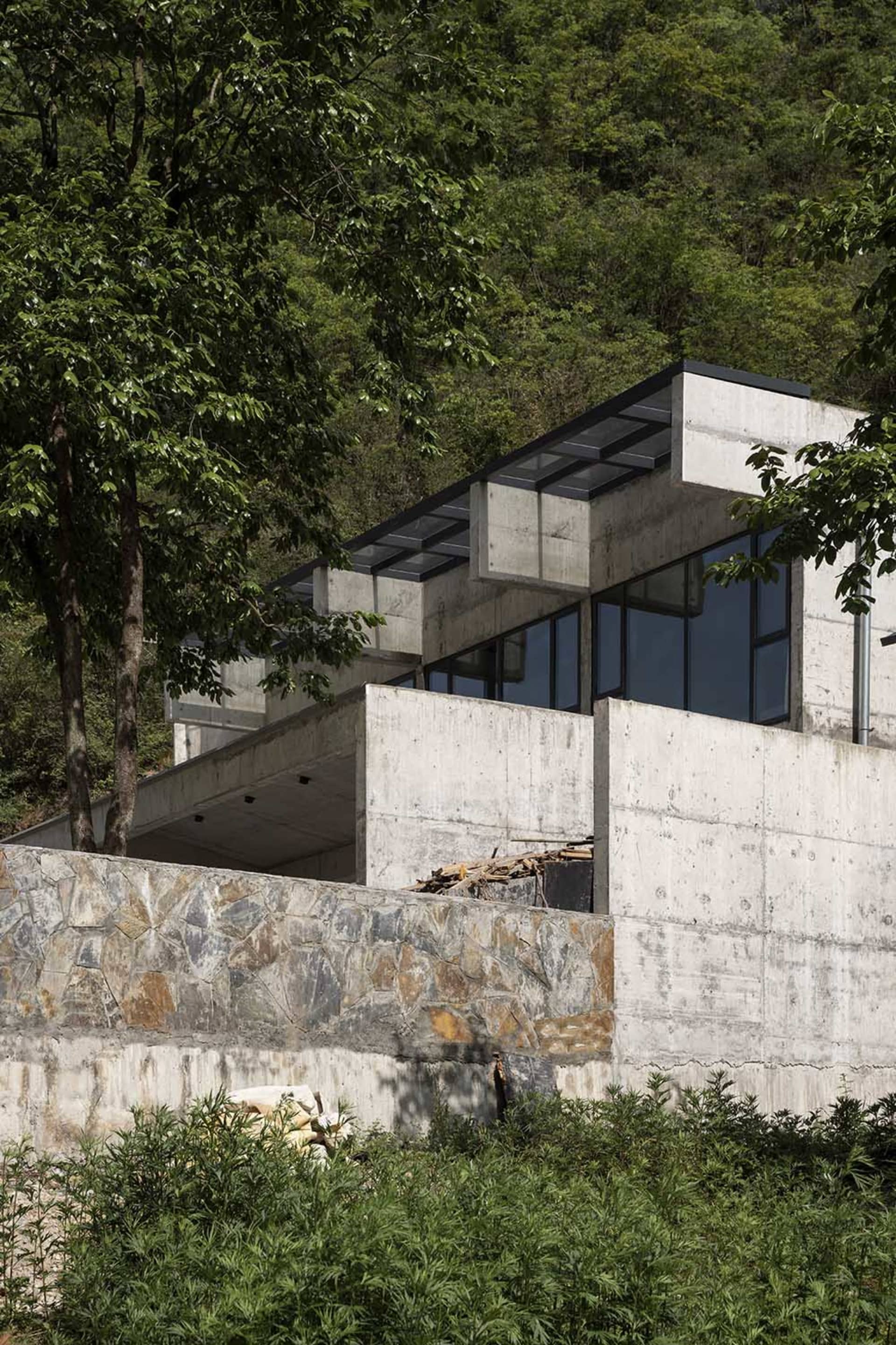 一座現代極簡住宅,外牆採用混凝土材質,搭配大型窗戶,眺望青翠山坡。