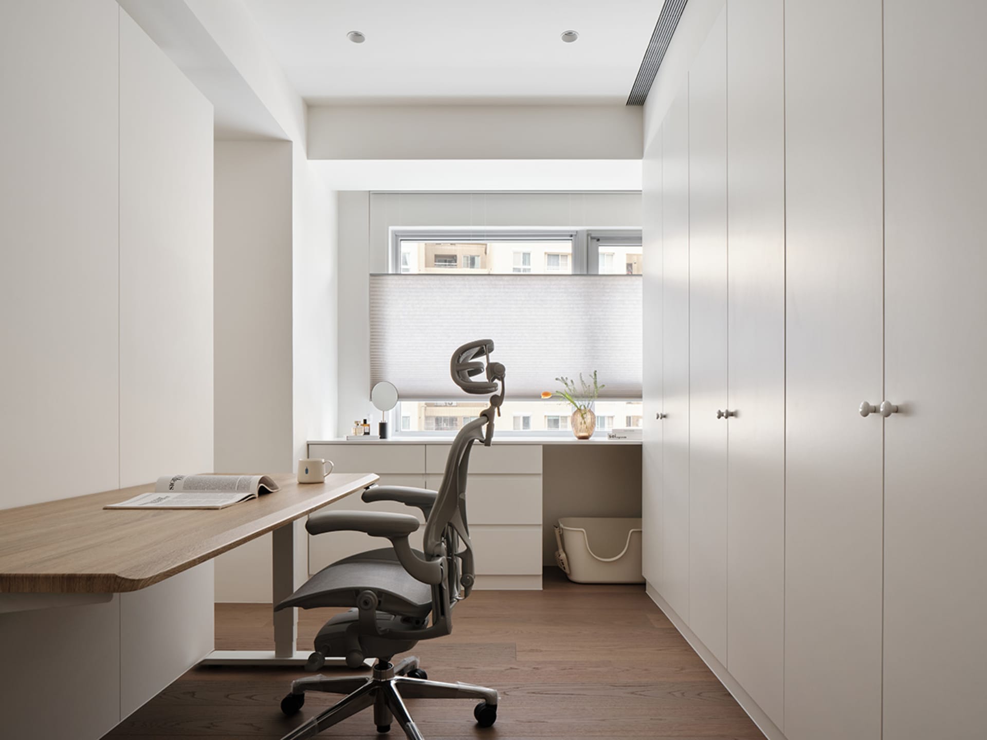 A modern minimalist home office featuring a wooden desk, glass window, and ergonomic chair.