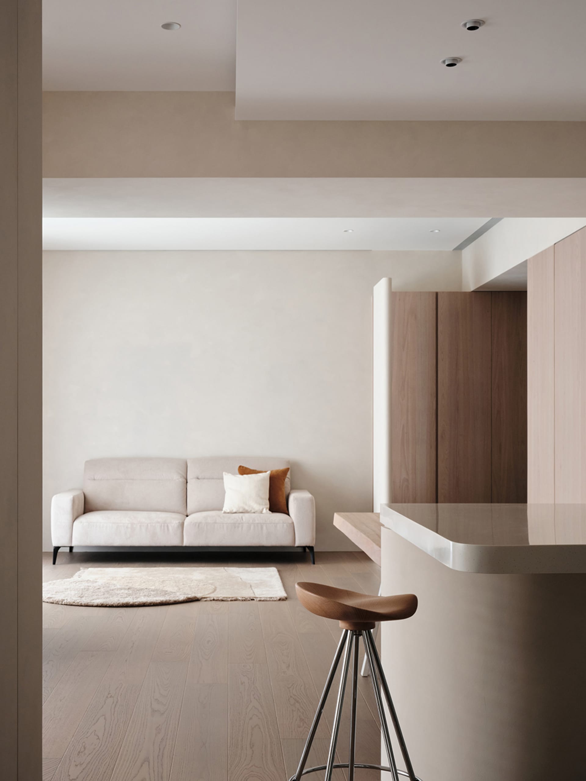 A modern living room with a minimalist design featuring neutral-colored furniture and wood floors.