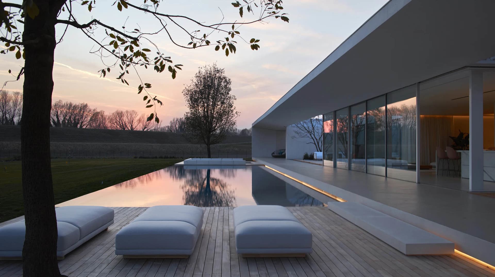 Modern house with glass walls and concrete patio during sunset.