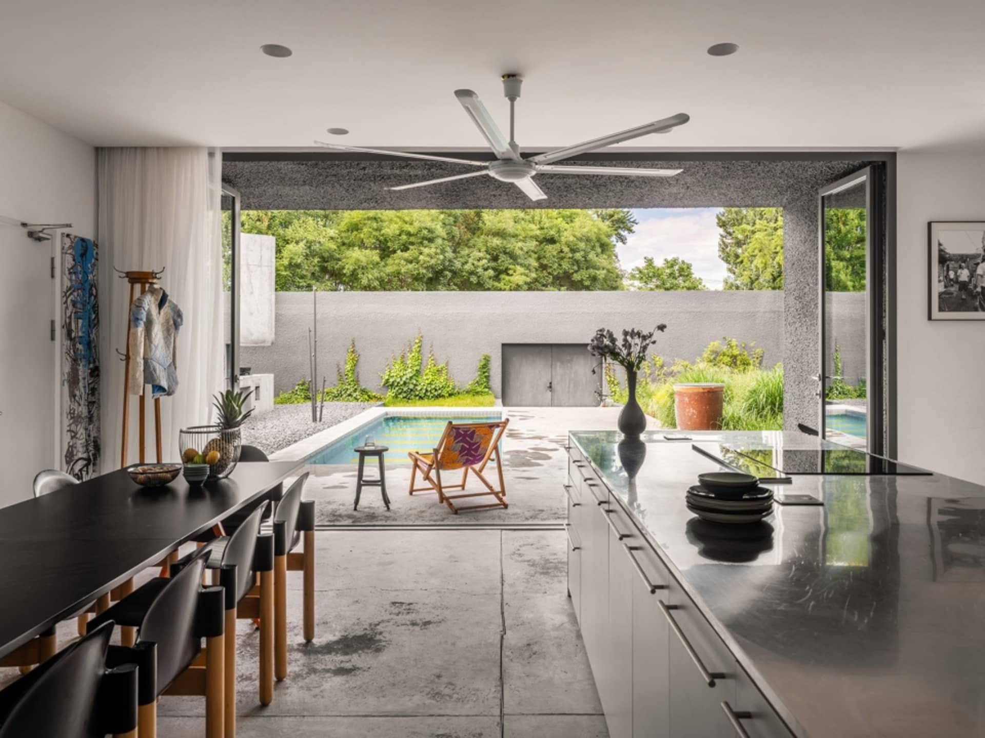 A modern kitchen with dark concrete countertops, wooden cabinets, and a glass backsplash, featuring a large table with chairs