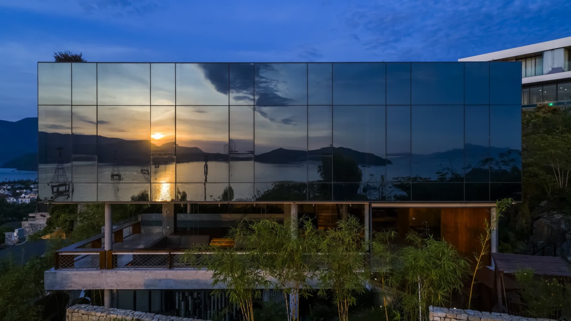 A modern house with a glass facade reflecting a beautiful sunset.
