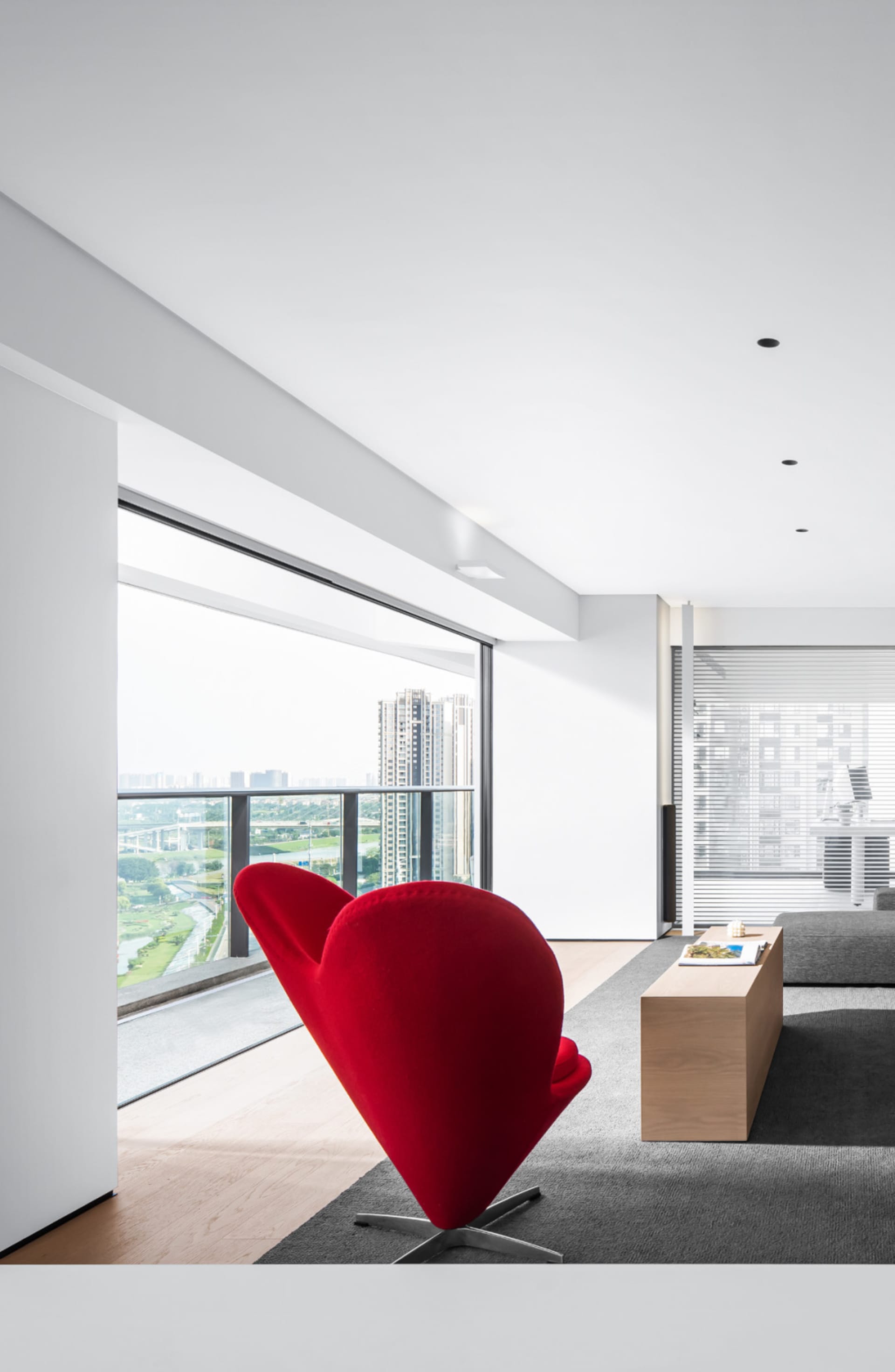 A modern living room featuring a striking red cone-shaped chair with a cityscape view through the floor-to-ceiling windows.