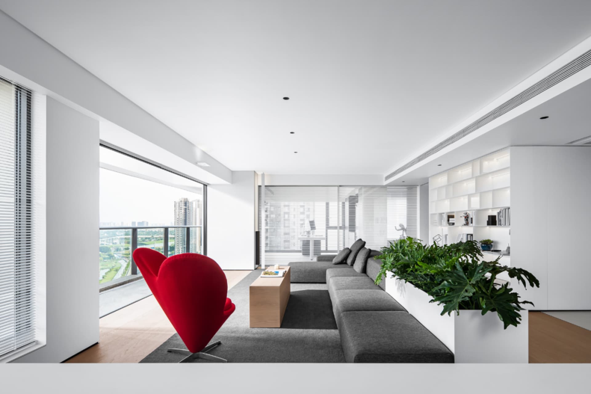 Contemporary living room featuring grey fabric sofa, red accent chair, large windows, and indoor green plant.