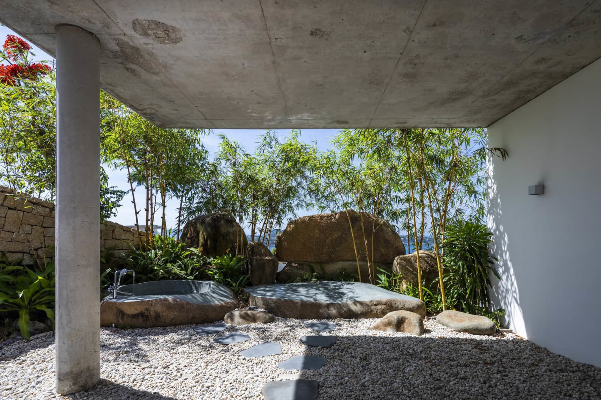 A sleek concrete outdoor bathroom with natural stone features and lush greenery.