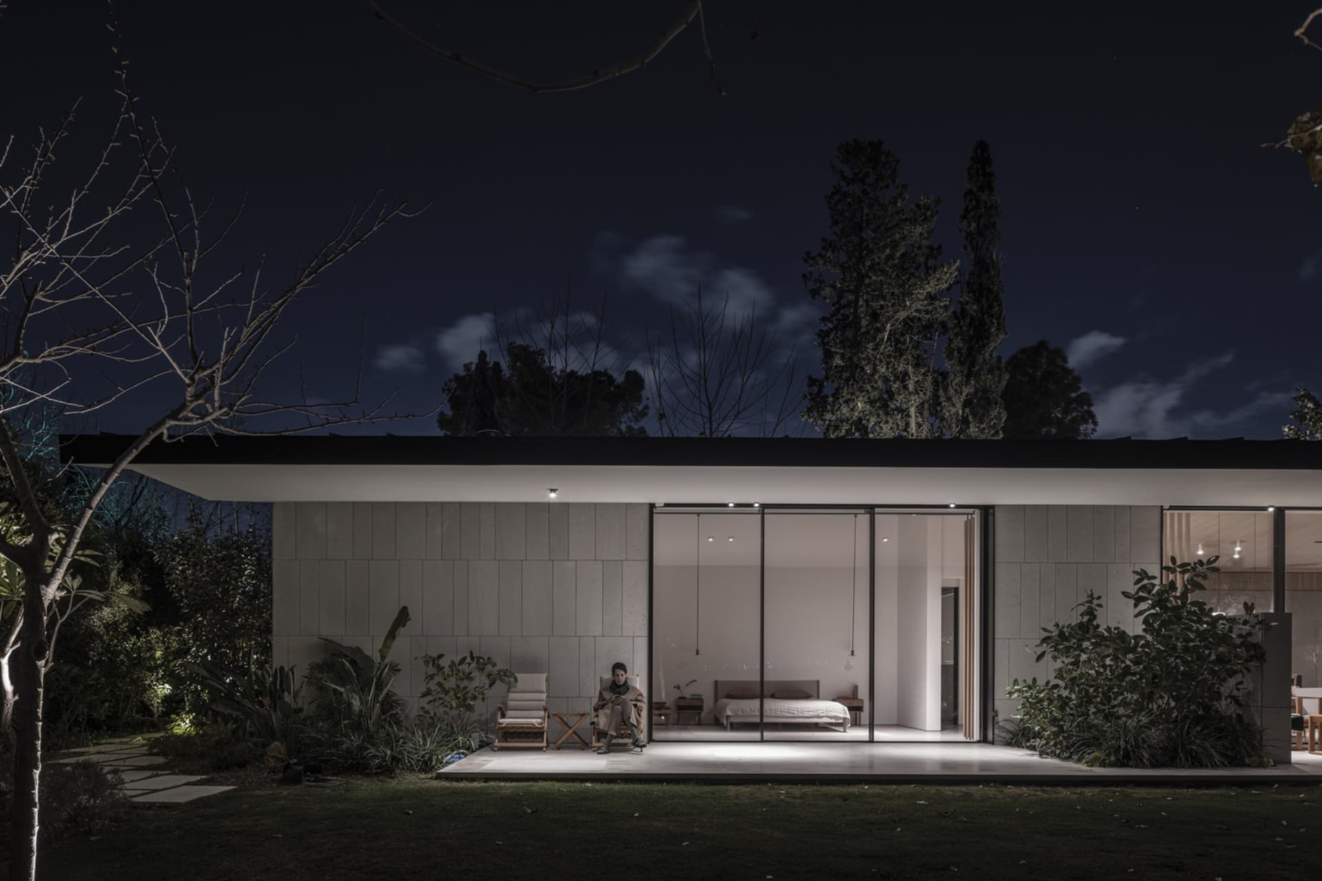 Modern residential exterior with concrete and glass materials, featuring a patio area at night.