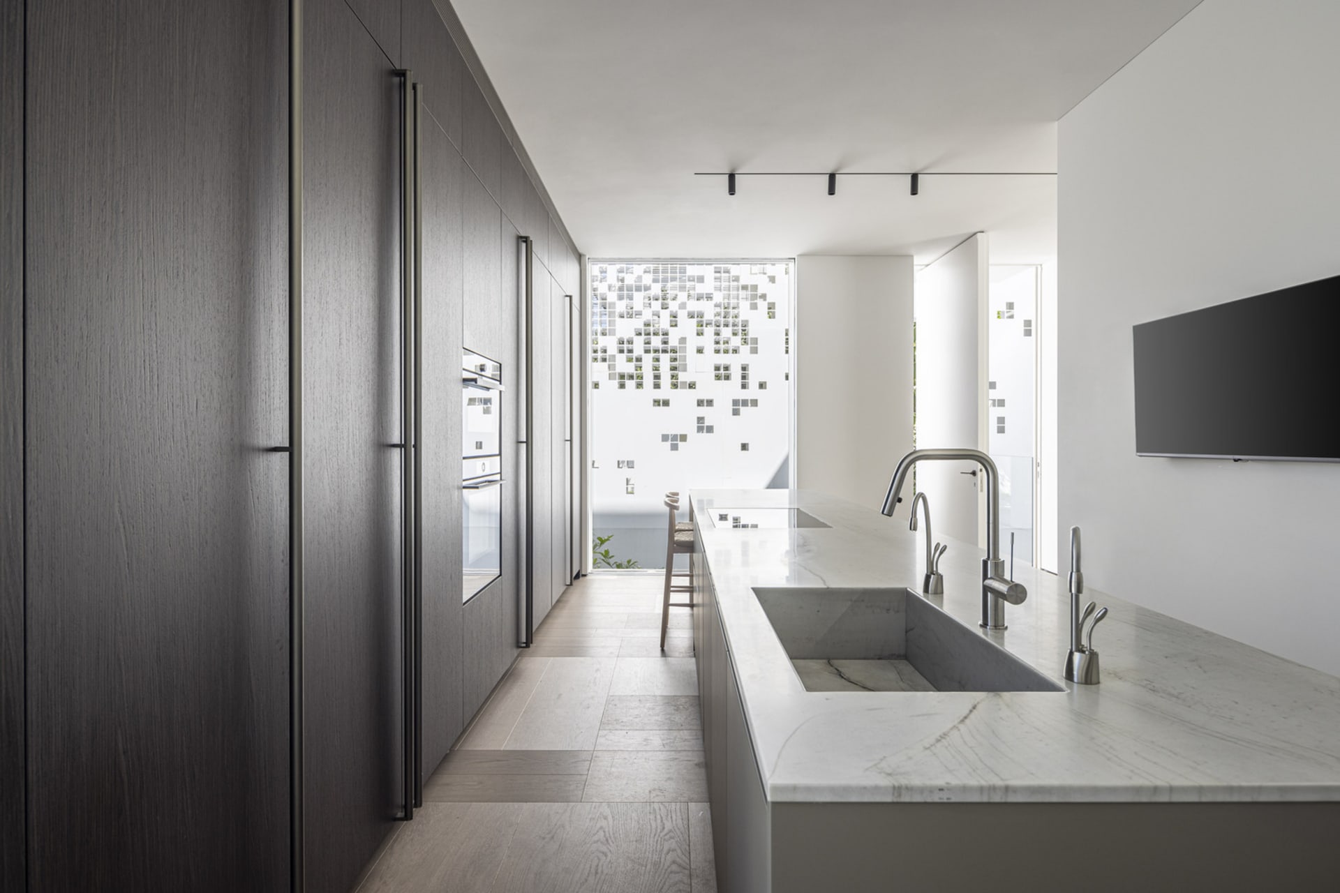 A modern minimalist kitchen featuring concrete and marble materials, with a white marble countertop and dark wooden cabinets.