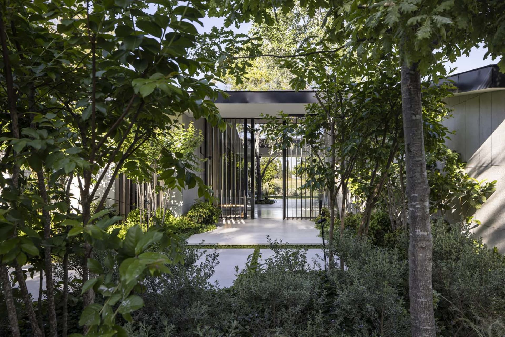 A modern residential entrance framed by greenery and metal gates, offering a serene and inviting atmosphere.