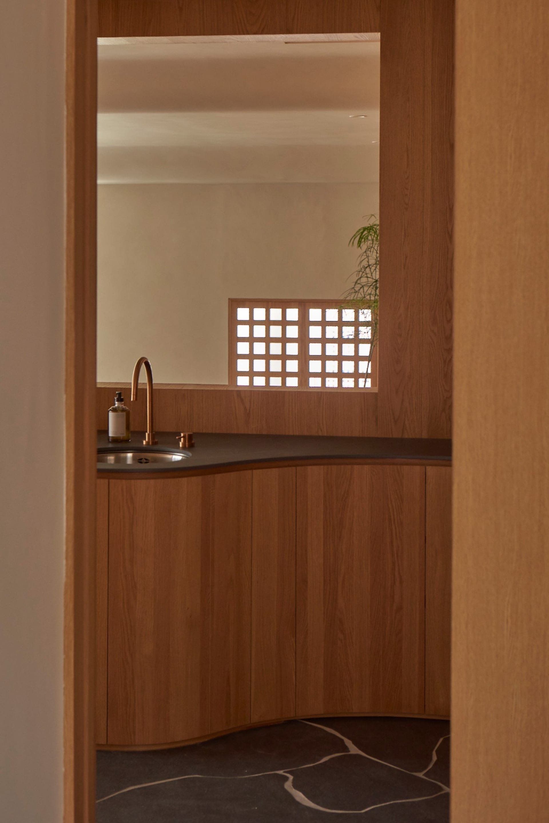 A modern kitchen interior with wooden cabinets, a black countertop, and a window with a latticed frame.