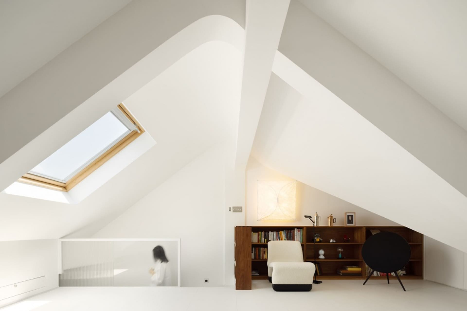 Well-designed minimalist attic with a skylight, wooden beam, and a bookshelf with a chair and a speaker.