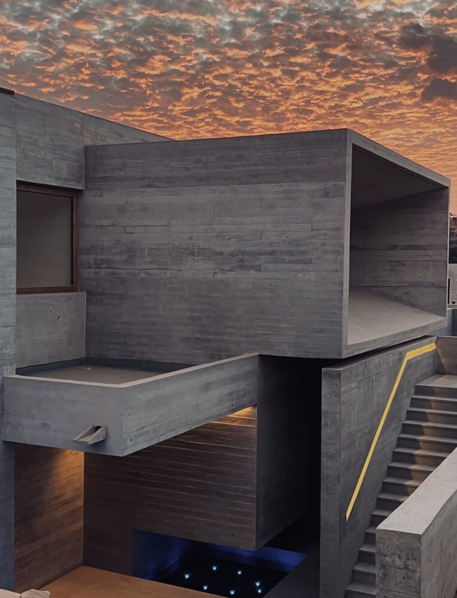 A modern, concrete exterior building with a sunset sky in the background.