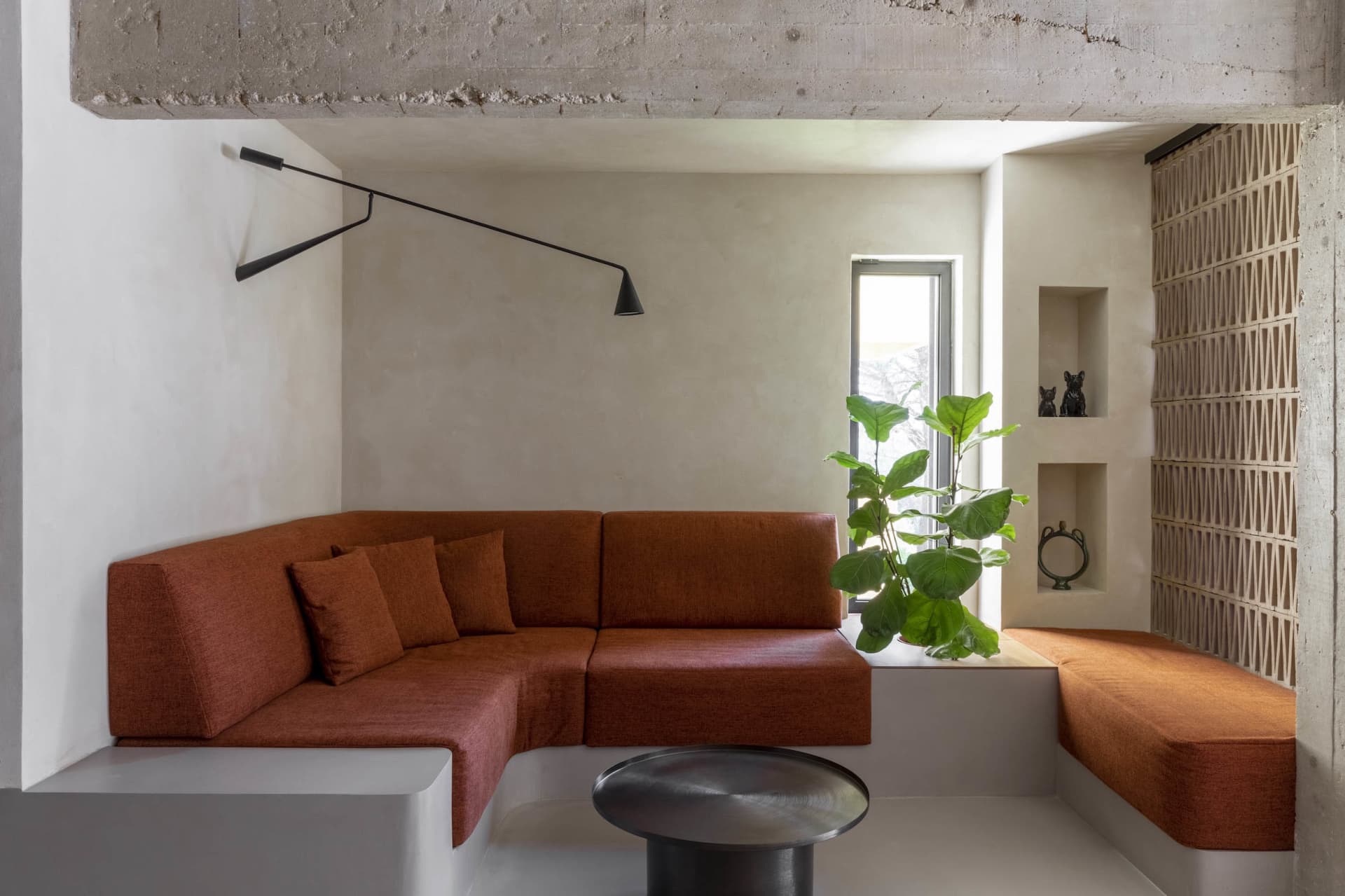Modern living room with orange sectional sofa, concrete walls, and indoor plants.