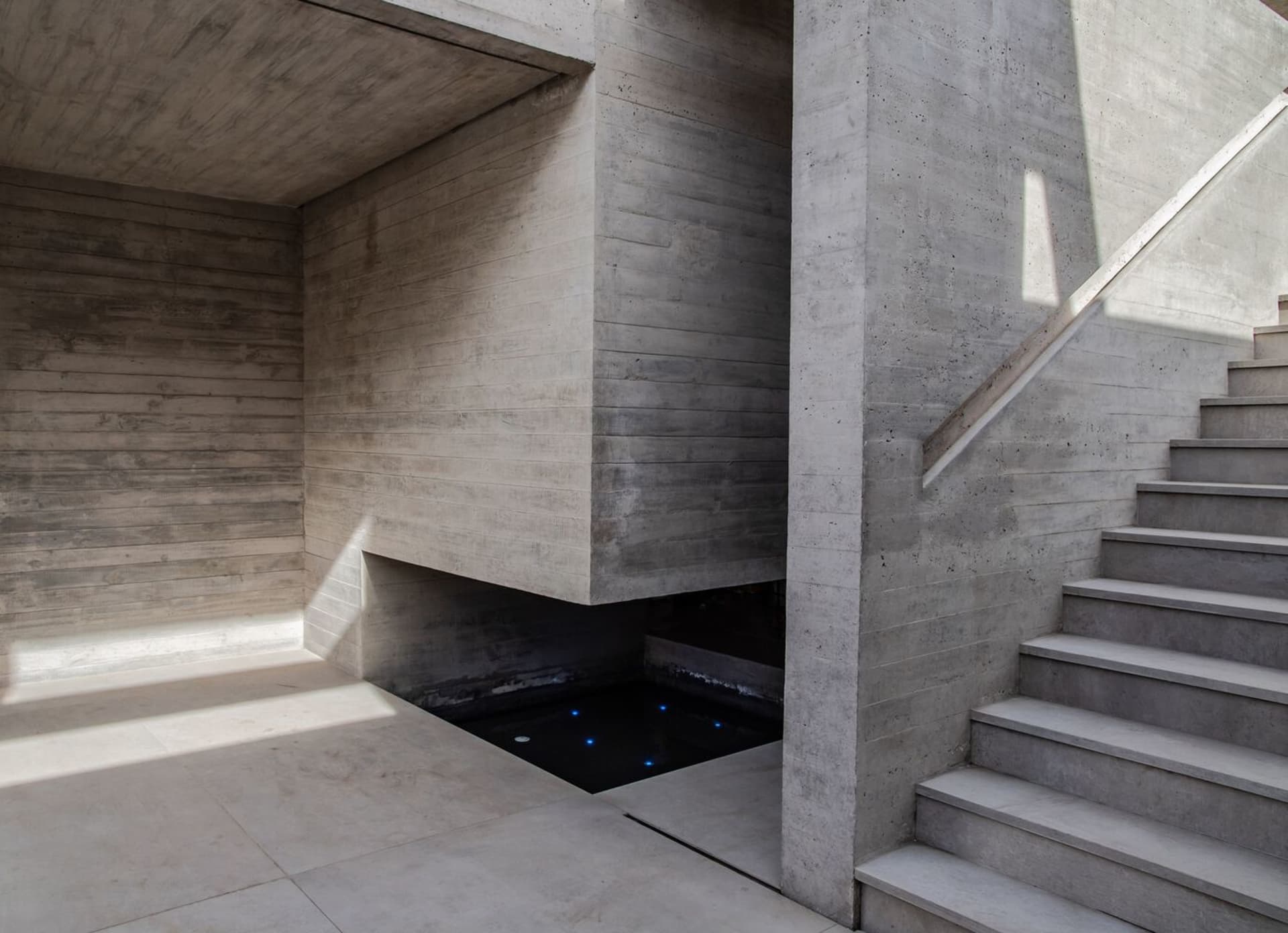 Modern staircase with concrete walls and steps, illuminated by sunlight.