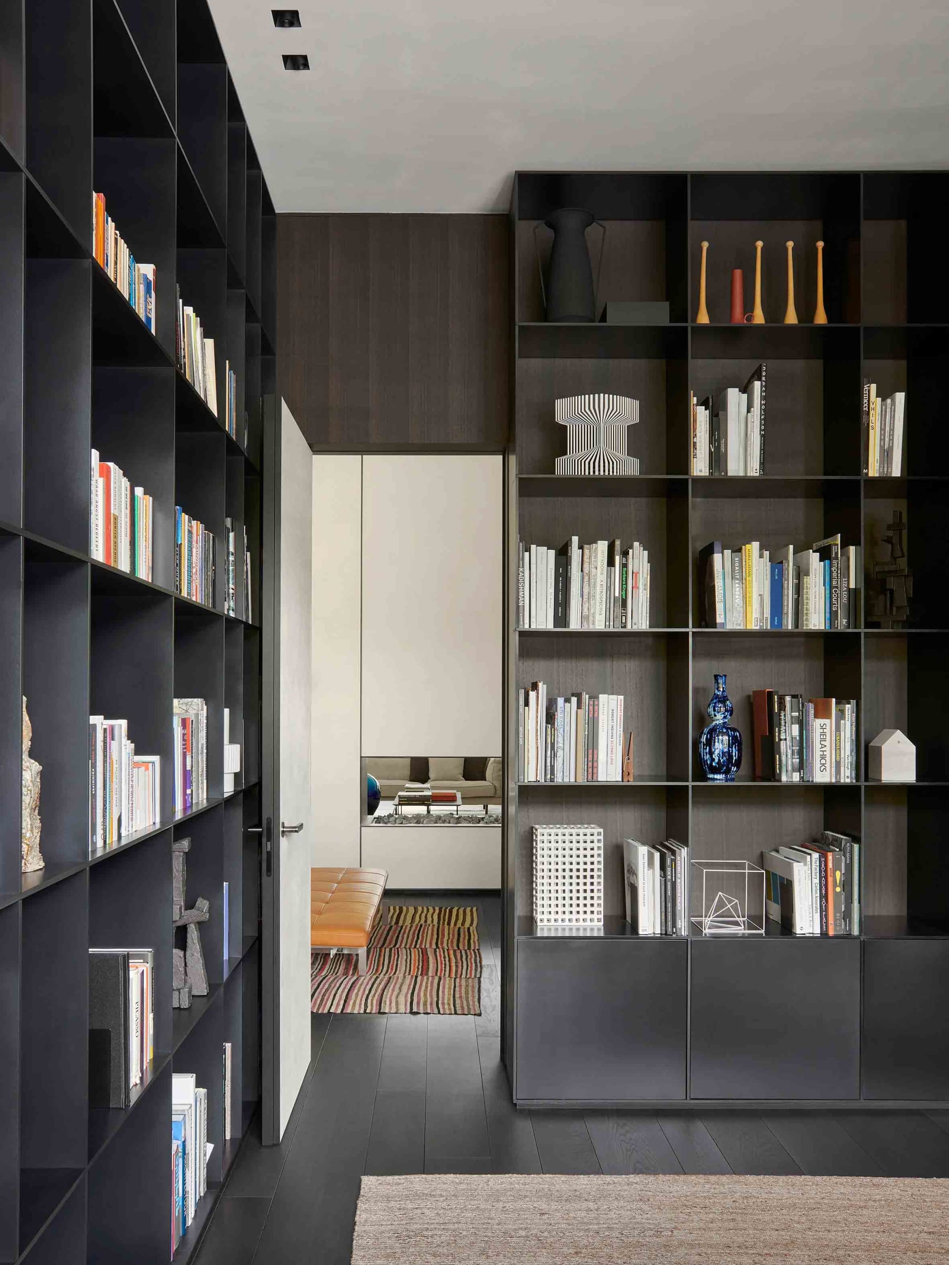 A modern library with dark wooden shelves filled with books and decorative items, featuring a minimalist design with sleek li