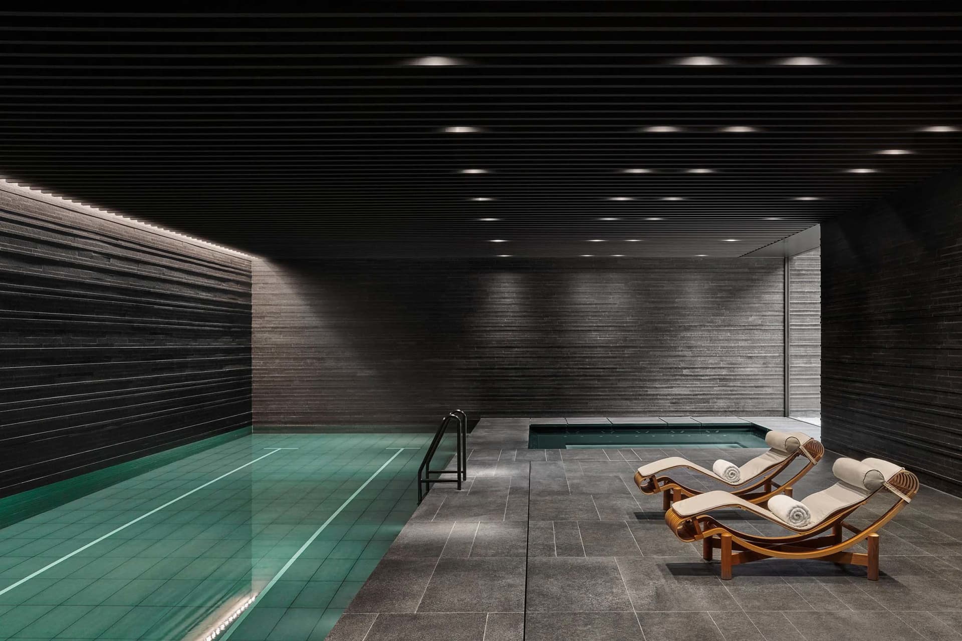 Modern indoor swimming pool with concrete walls, tiled bottom, and concrete deck.