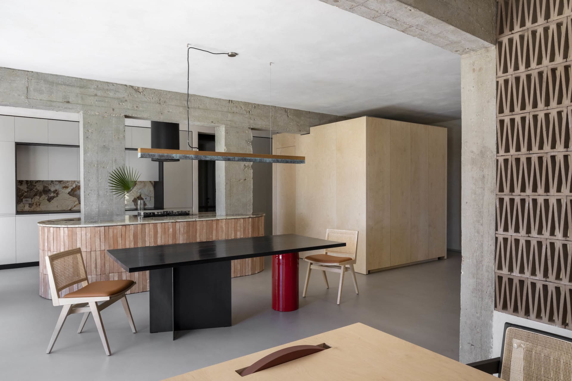 Modern dining room with concrete flooring, wooden table and chairs, and a metal pendant light hanging over the table.