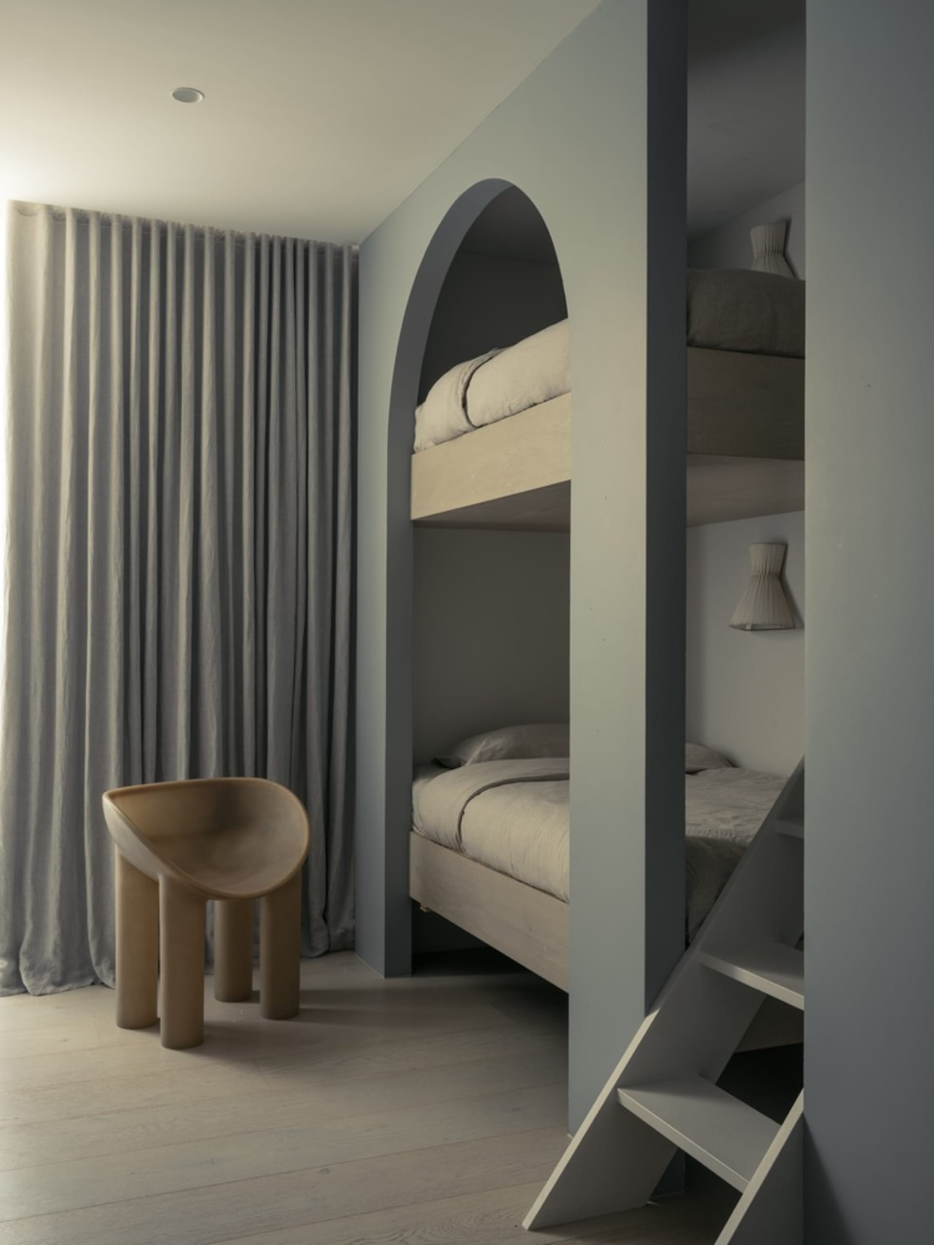 Modern minimalist bedroom featuring wood bunk beds with gray curtains and a unique brown tube-shaped chair.