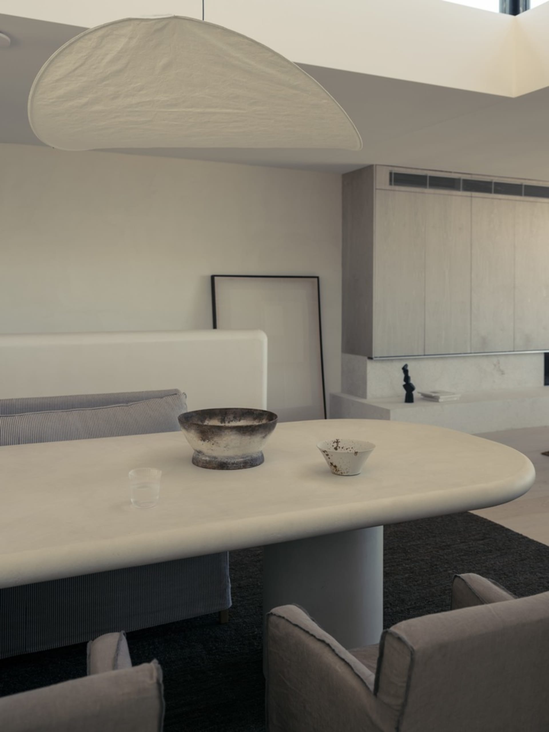 A minimalist dining room featuring a concrete table, chairs, and bowl with another bowl nearby.
