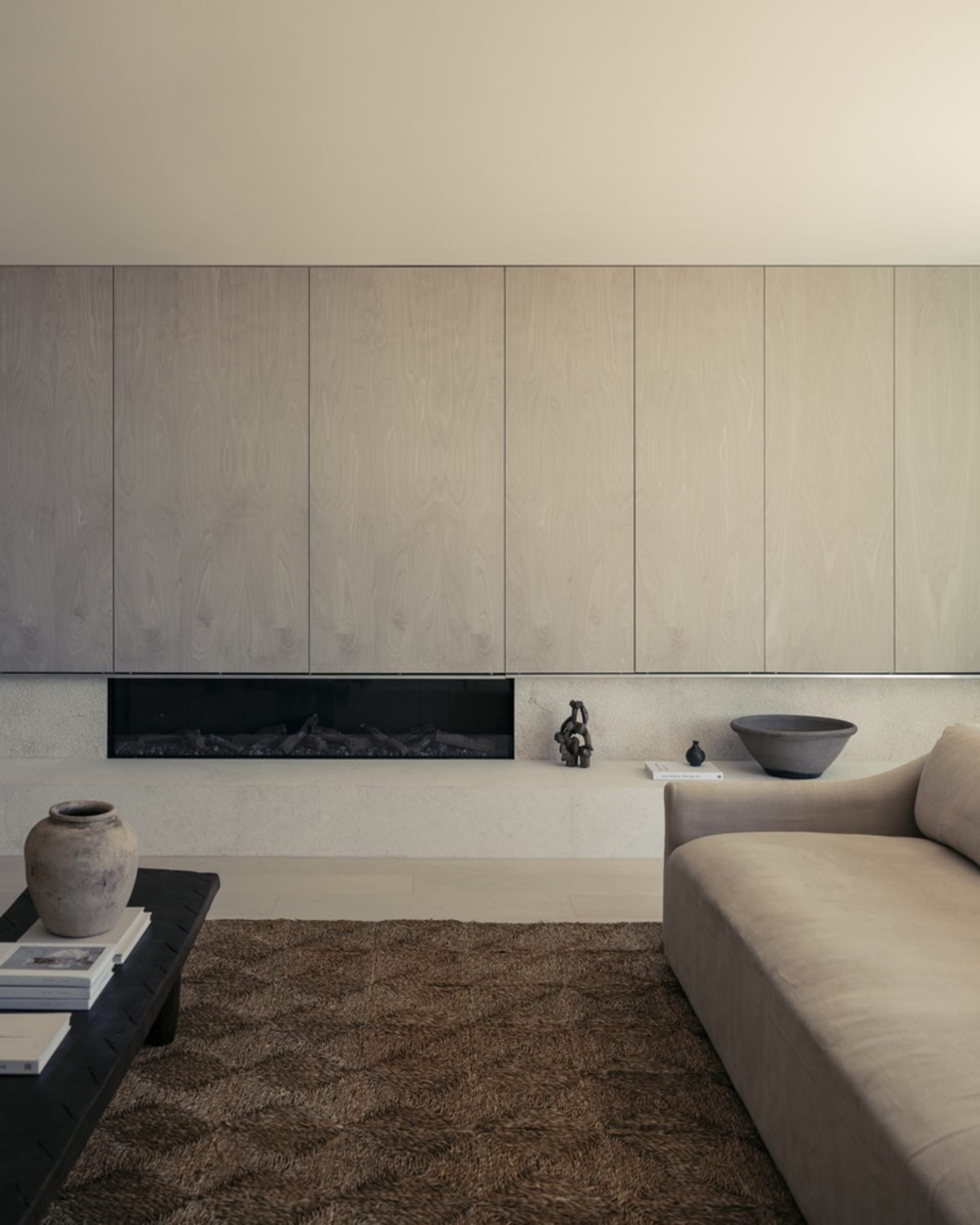A modern minimalist living room with neutral-toned materials and a sleek, wooden wall.