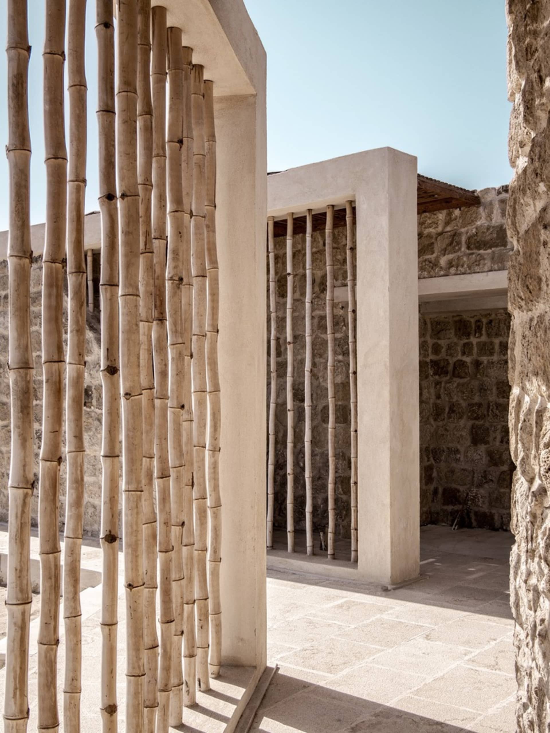 A modern architectural structure featuring tall wooden poles and stone walls.