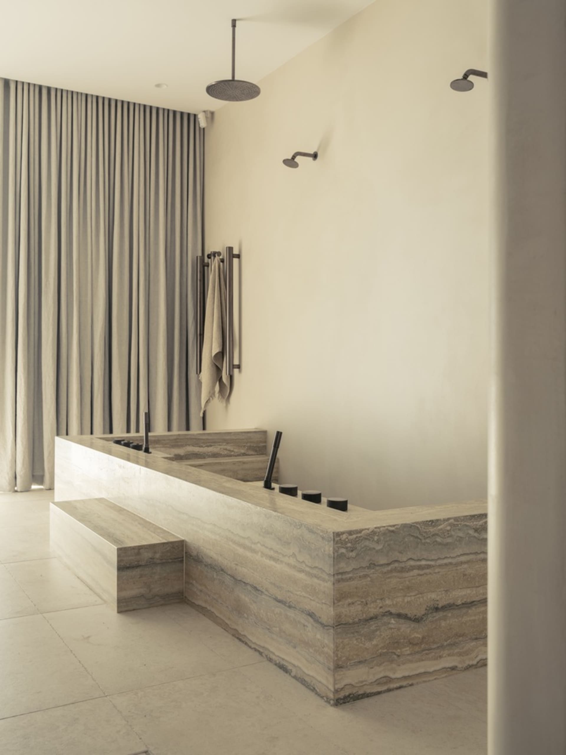 A minimalist marble bathroom with a large freestanding bathtub, modern fixtures, and a frosted glass shower door.