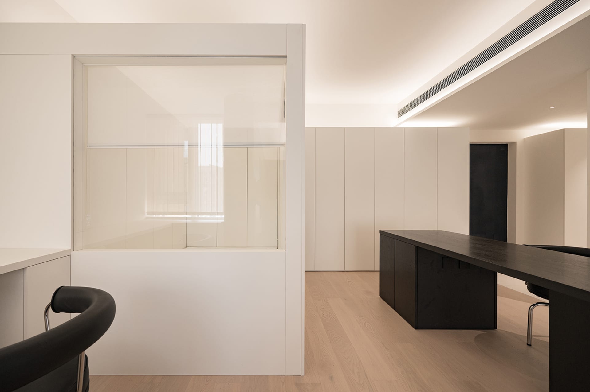 Modern minimalist office space featuring sleek white concrete walls and black furniture.