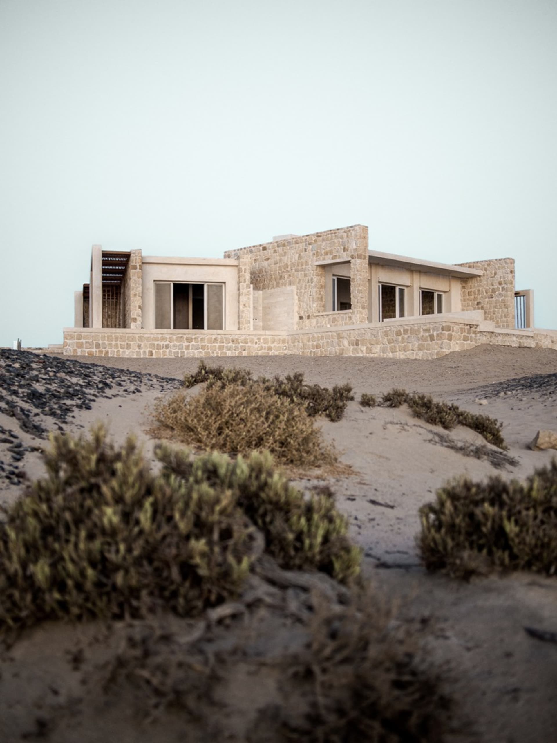 A modern residential house constructed with stone materials, featuring large windows and an open, airy design.