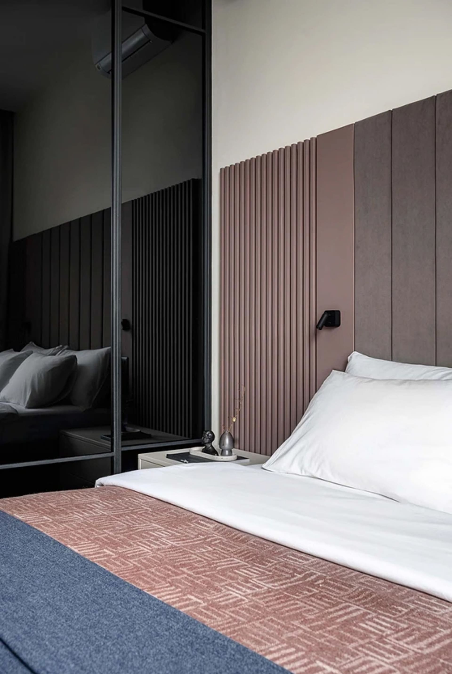 A neatly made bed with a textured cover and a white pillow, against a modern headboard with vertical lines.