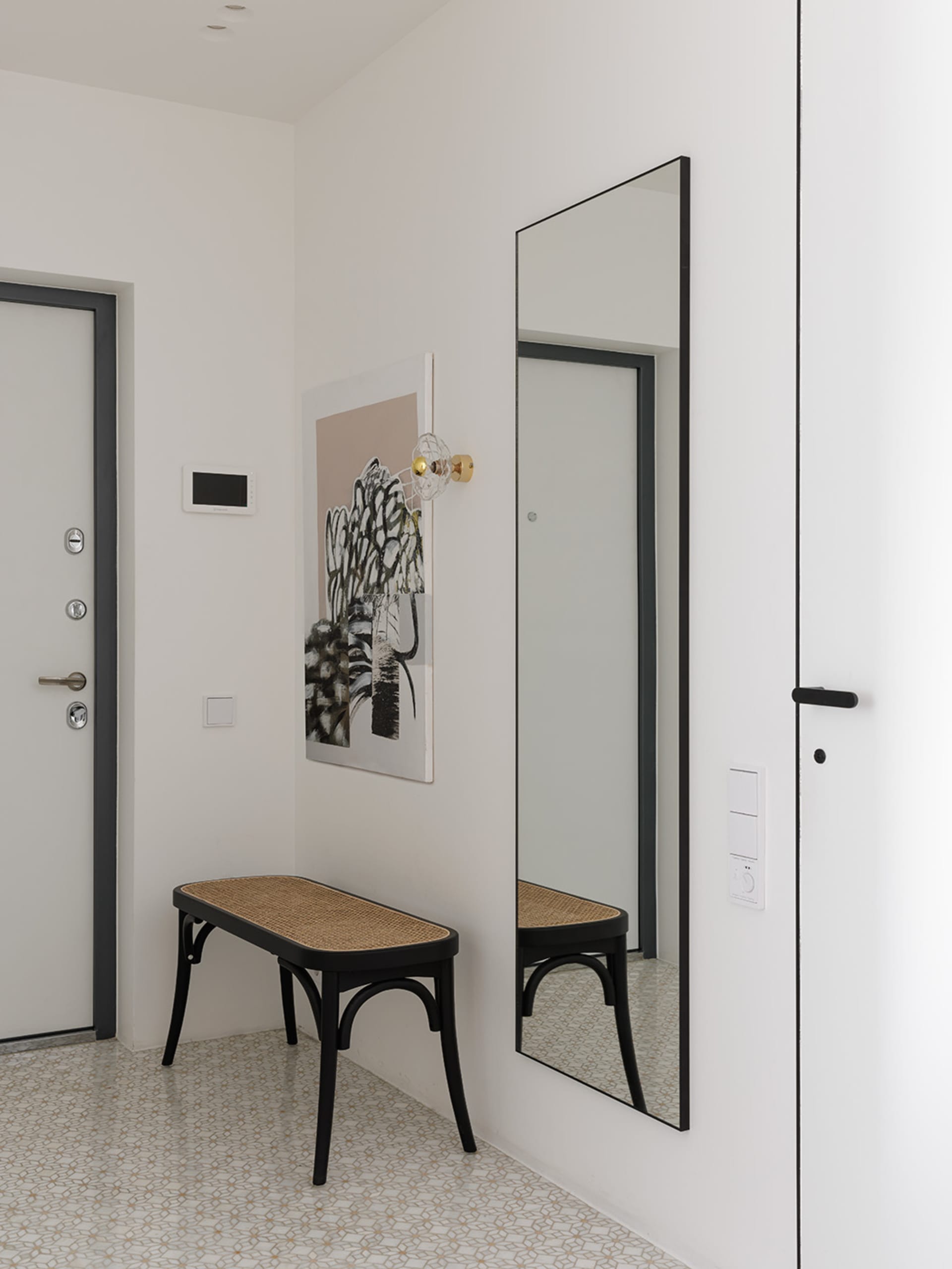 A minimalist entrance hall featuring a black-framed floor-to-ceiling mirror, a black and wicker bench, and a modern light fix