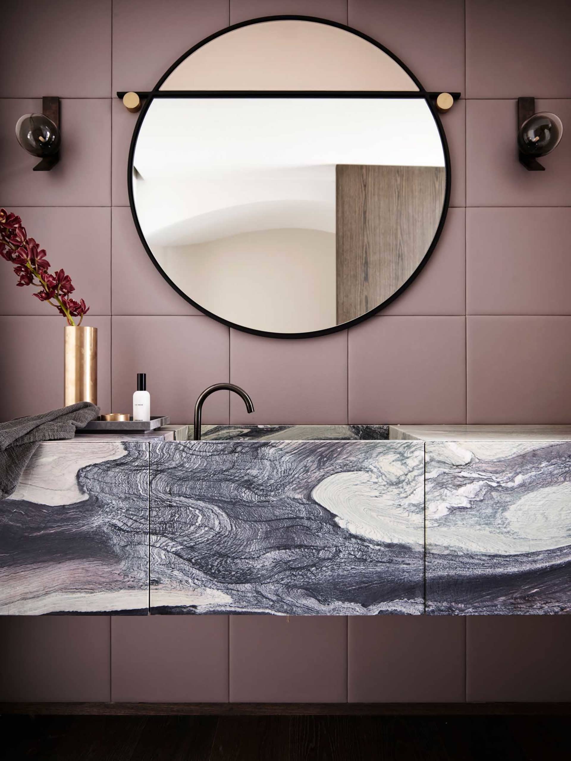 A modern bathroom featuring a marble sink counter and a round mirror.