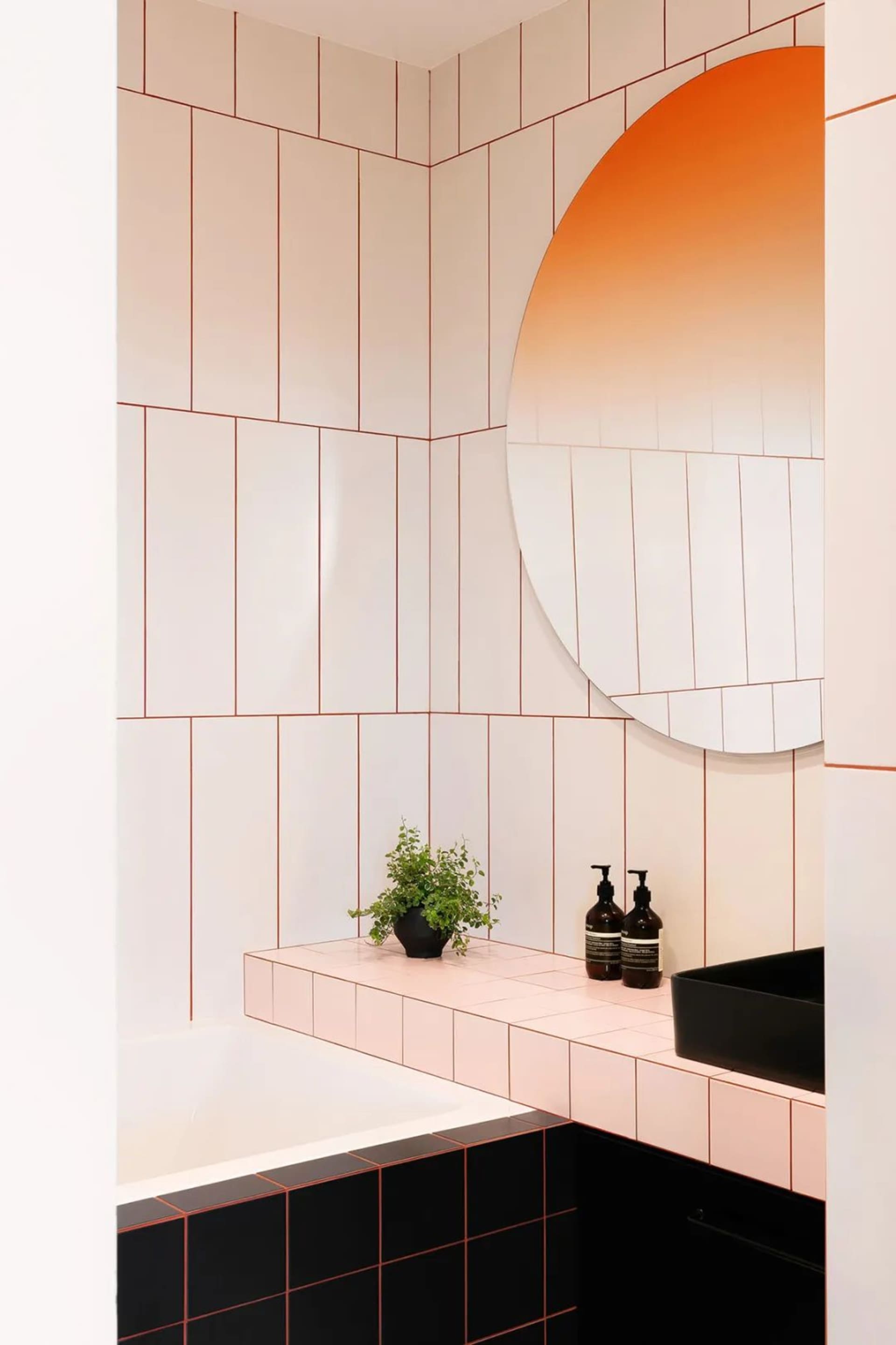 Modern bathroom with large black and white ceramic tiles, black countertop, and orange-hued wall above