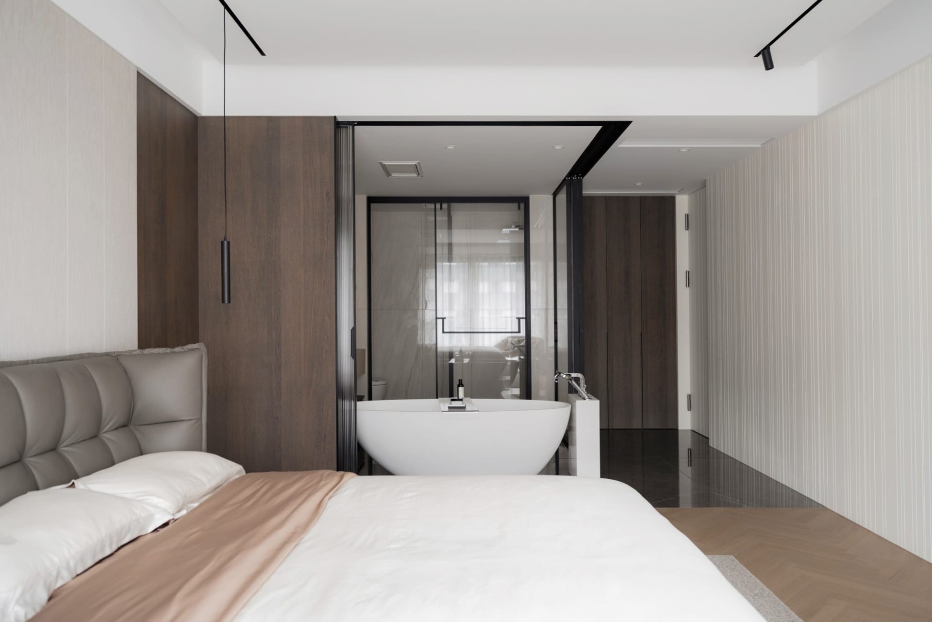 A modern bedroom featuring a bed with a grey headboard, a white and wooden floor, a marble bathtub, and wooden walls.