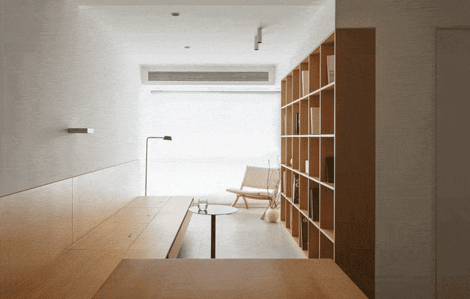 Modern minimalist living room featuring a large wooden bookshelf and a simple wooden table with a clear glass top.