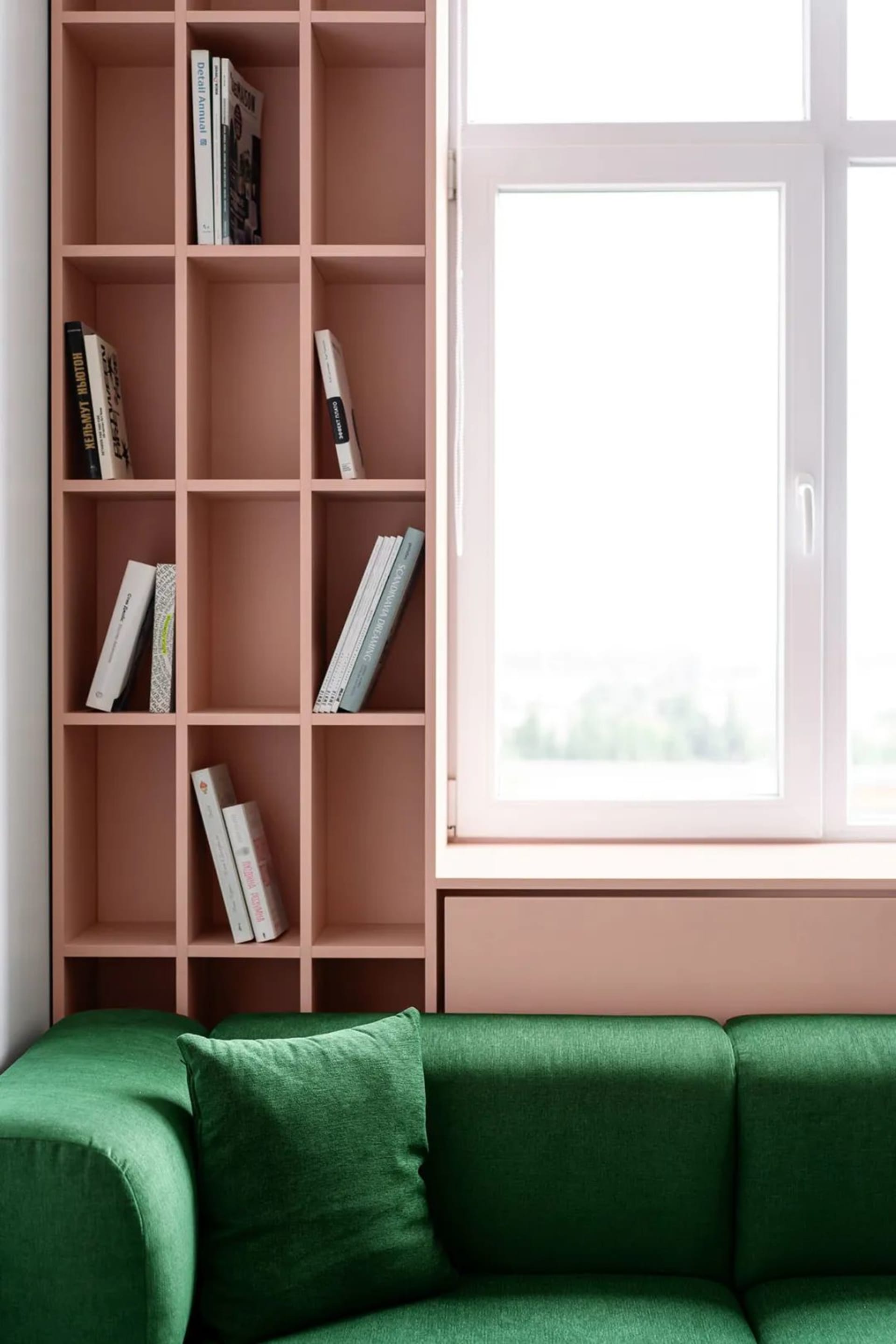 A modern living room featuring a green sofa with a bookshelf and a window.