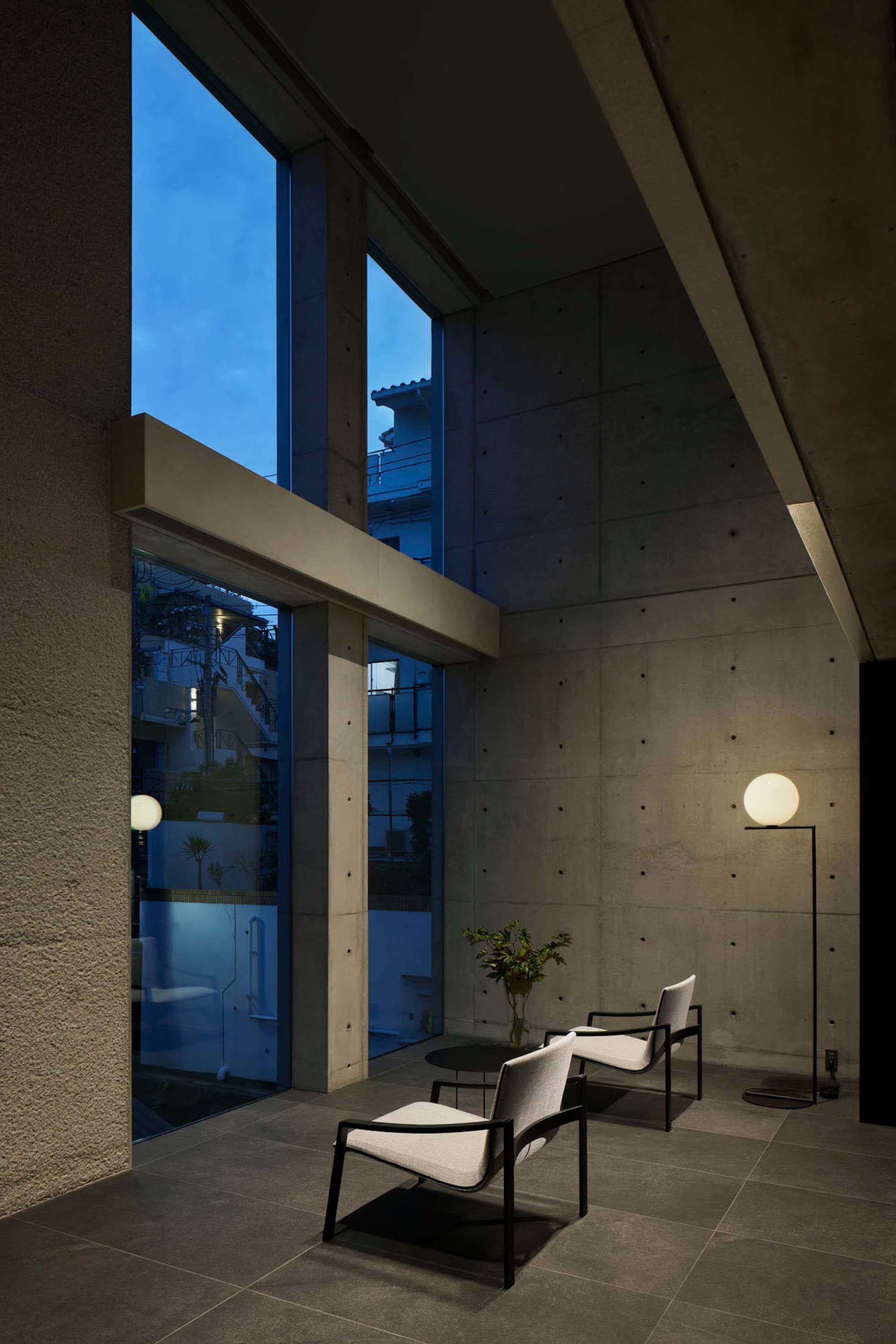 A modern interior living room featuring minimalist design with concrete walls and floor, large windows, and two armchairs.