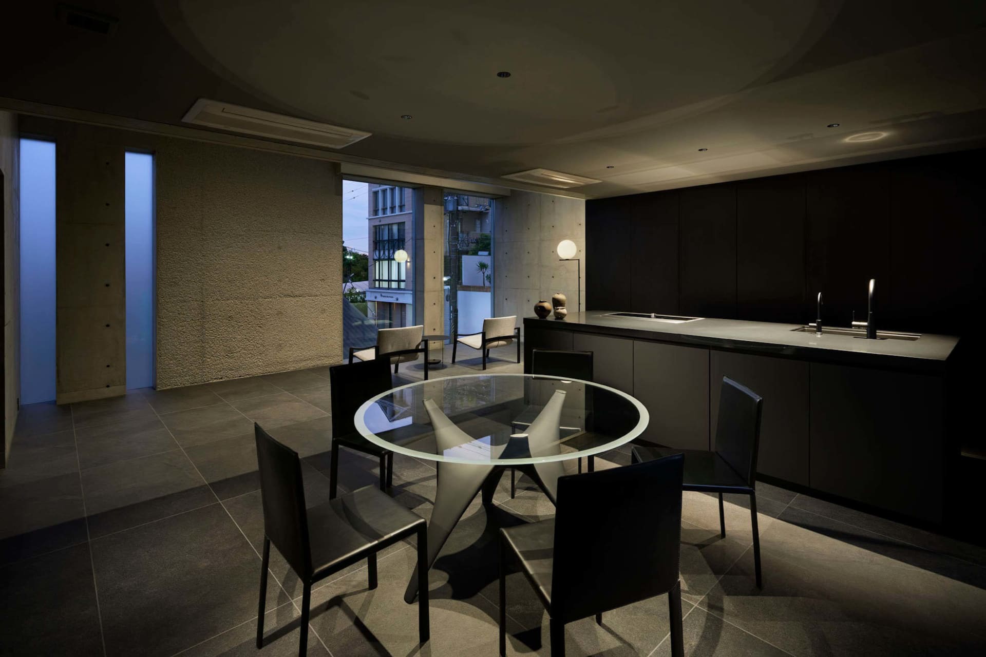 Modern kitchen and dining area with dark wood, concrete, and glass materials.