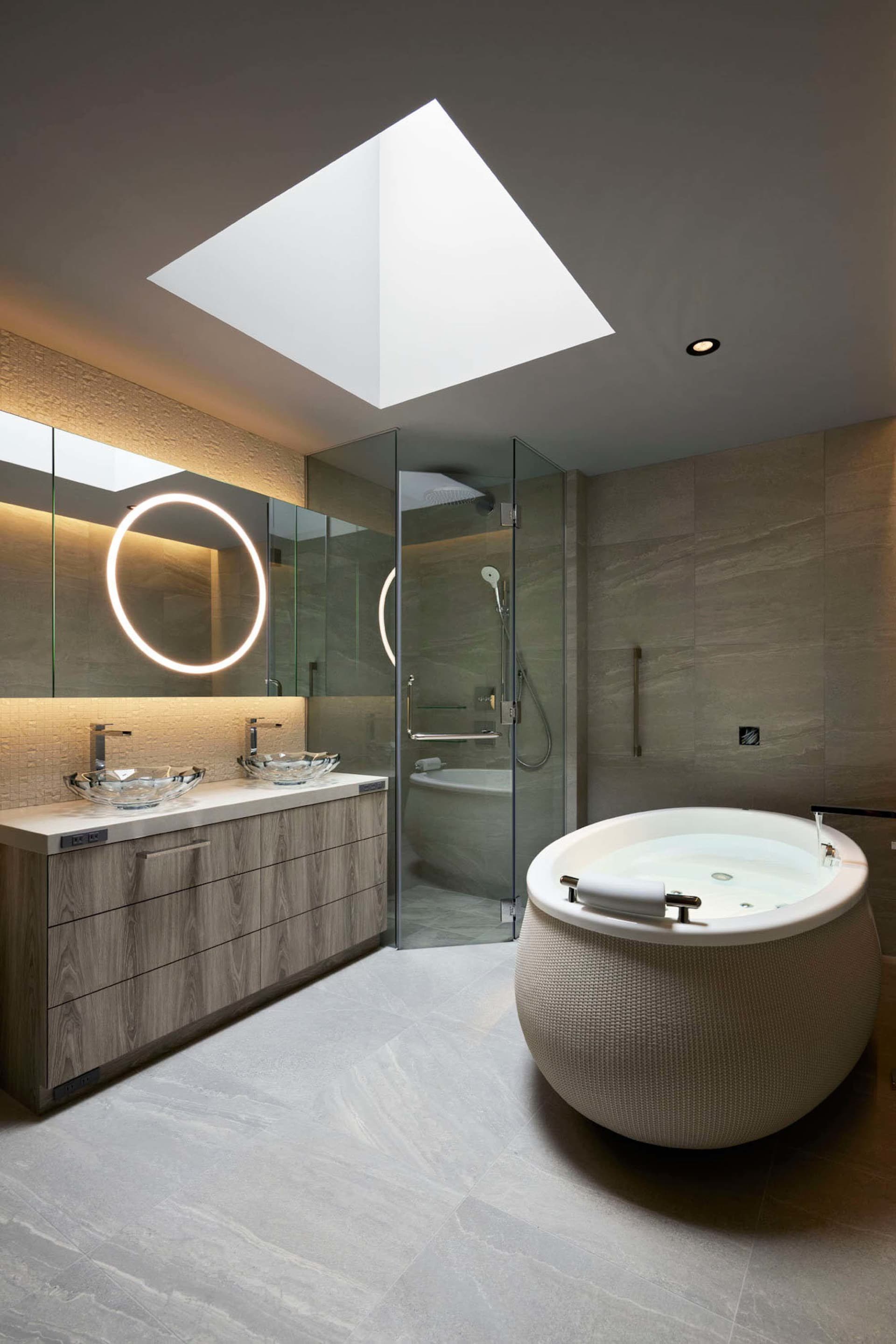 Modern master bathroom suite featuring a ceramic tile floor, freestanding tub, glass shower enclosure, and double vanity with