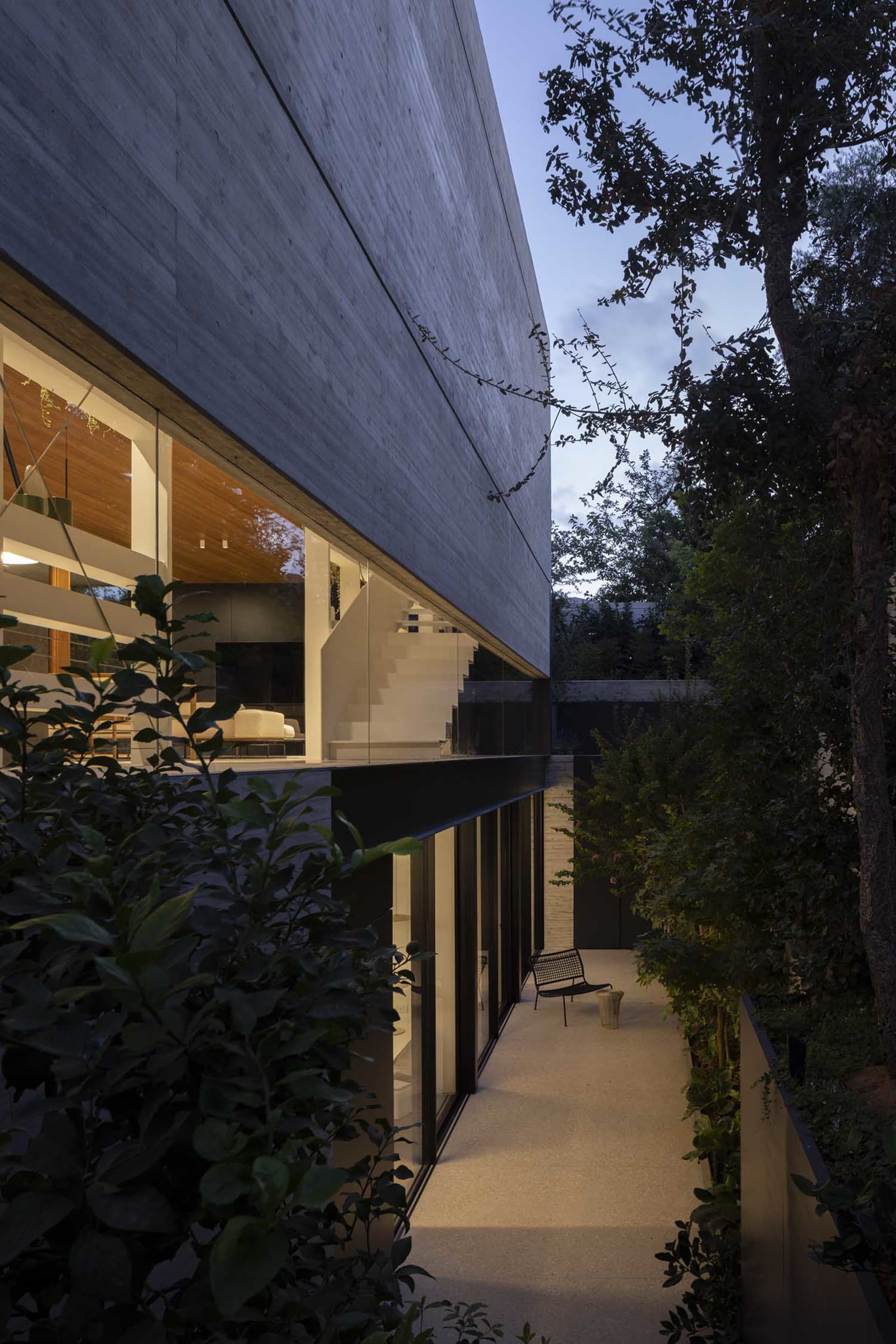 Modern concrete exterior of a house with large windows and garden at dusk.