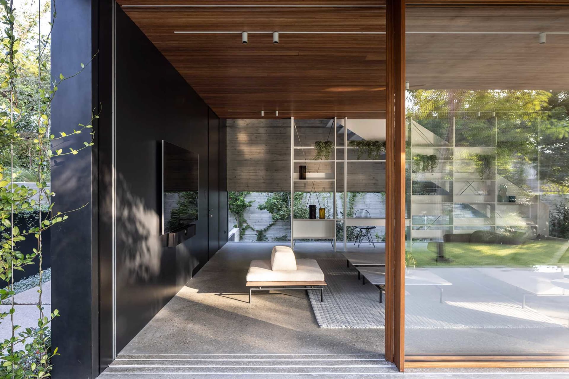 Modern living room with minimalist furniture and glass walls providing a connection to the outdoor green space.