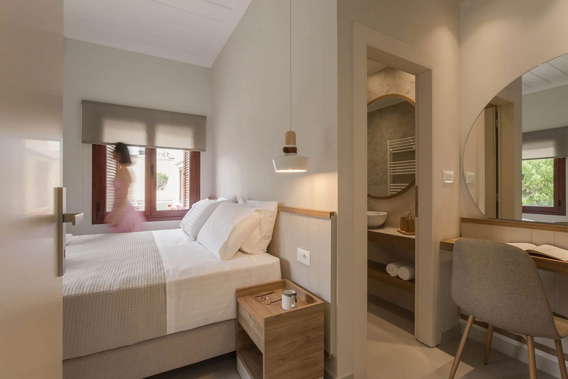 A minimalist bedroom with a white and neutral color theme, featuring a bed, nightstand, and bathroom access