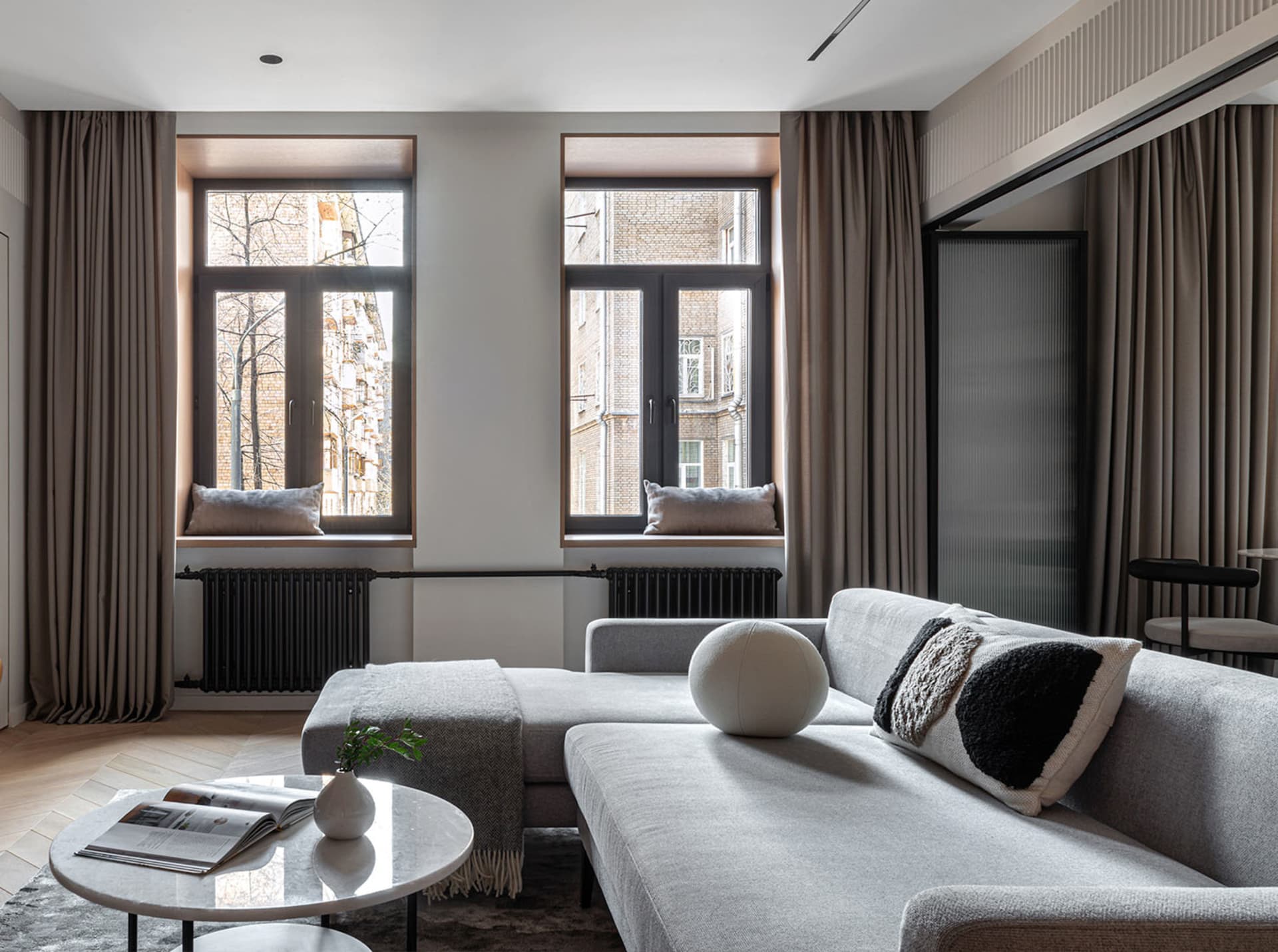 Modern living room with a grey sofa, round marble coffee table, fabric cushions, and a metal frame.