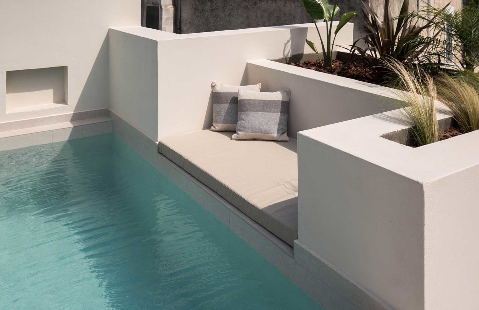 Modern, minimalist outdoor seating area with concrete walls and cushions by a pool.