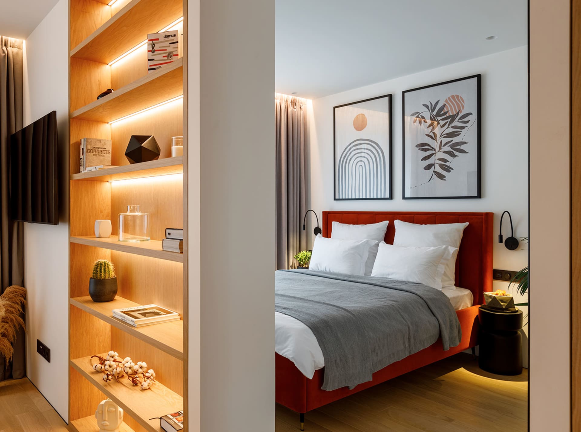 A cozy modern bedroom featuring a red upholstered bed with white pillows and a gray blanket, illuminated by warm under-shelf