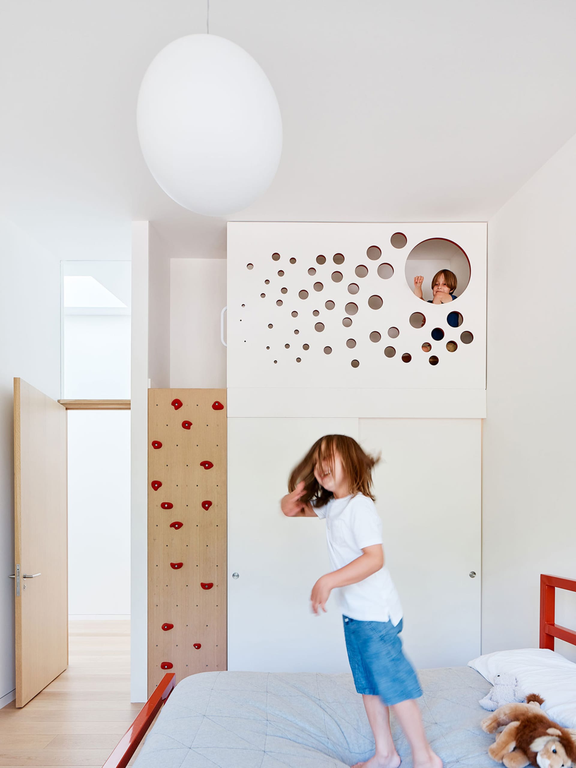 Children playing in a modern children's room with play space, climbing wall, and loft bed.