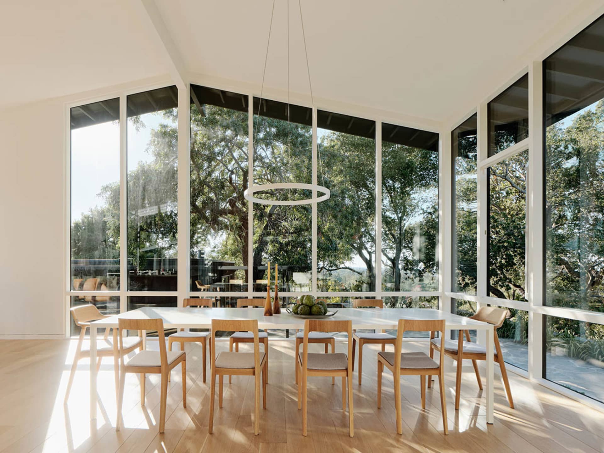 A modern dining room featuring a large table surrounded by wooden chairs, with a hanging circular light fixture and large win