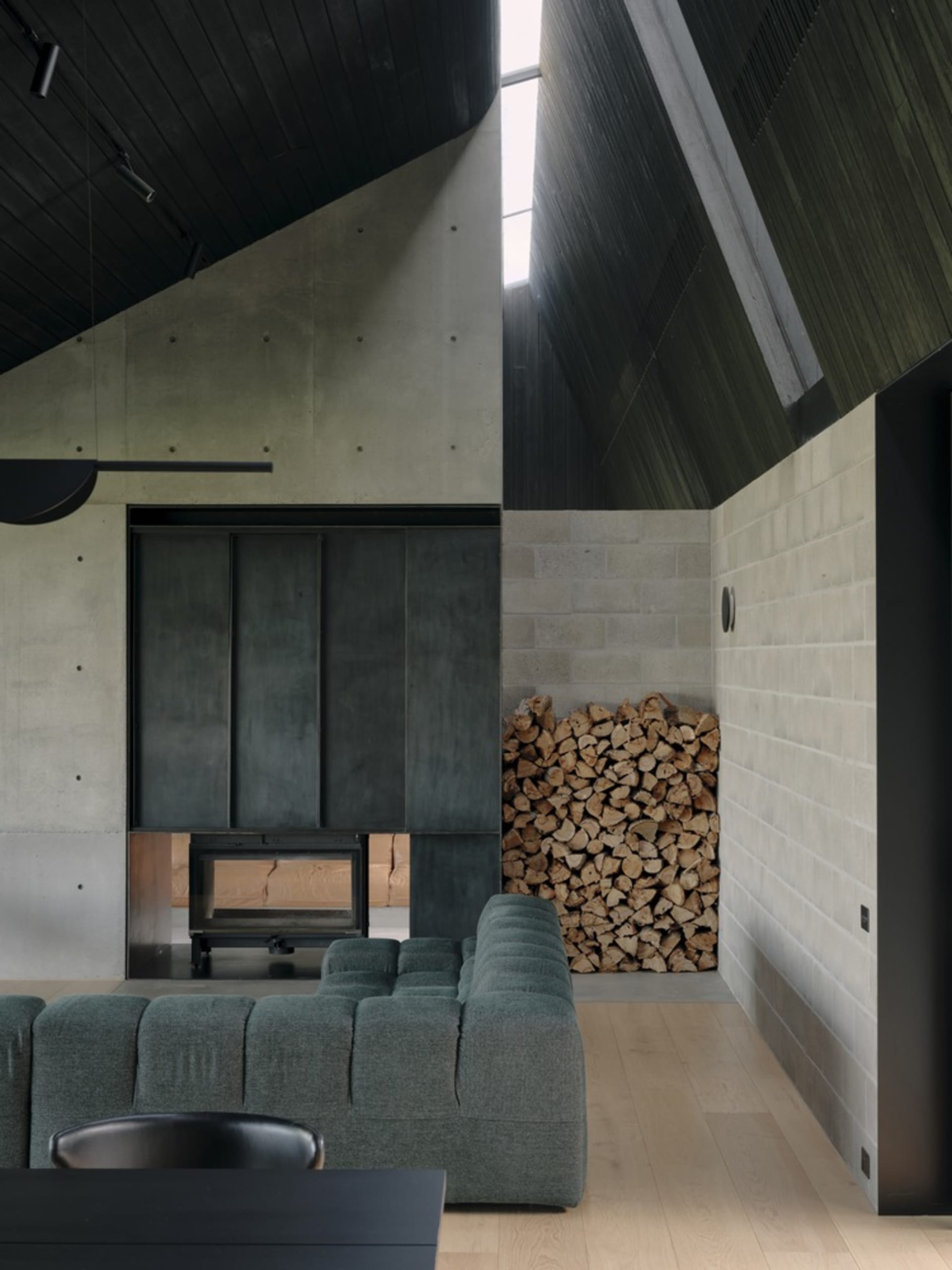 A spacious industrial-style living room featuring a concrete fireplace and numerous stacked logs.