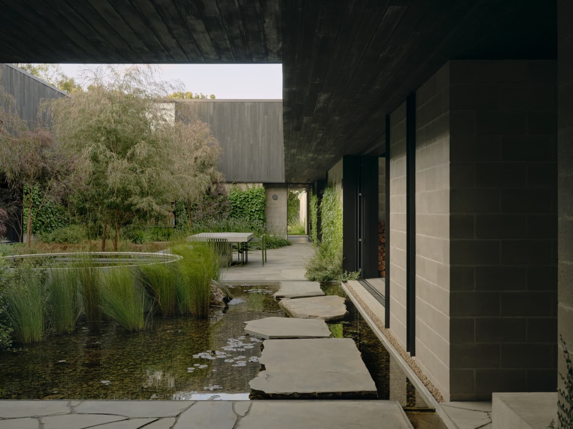 一座現代住宅擁有混凝土外觀,搭配花園、水景、步道與綠意植栽。