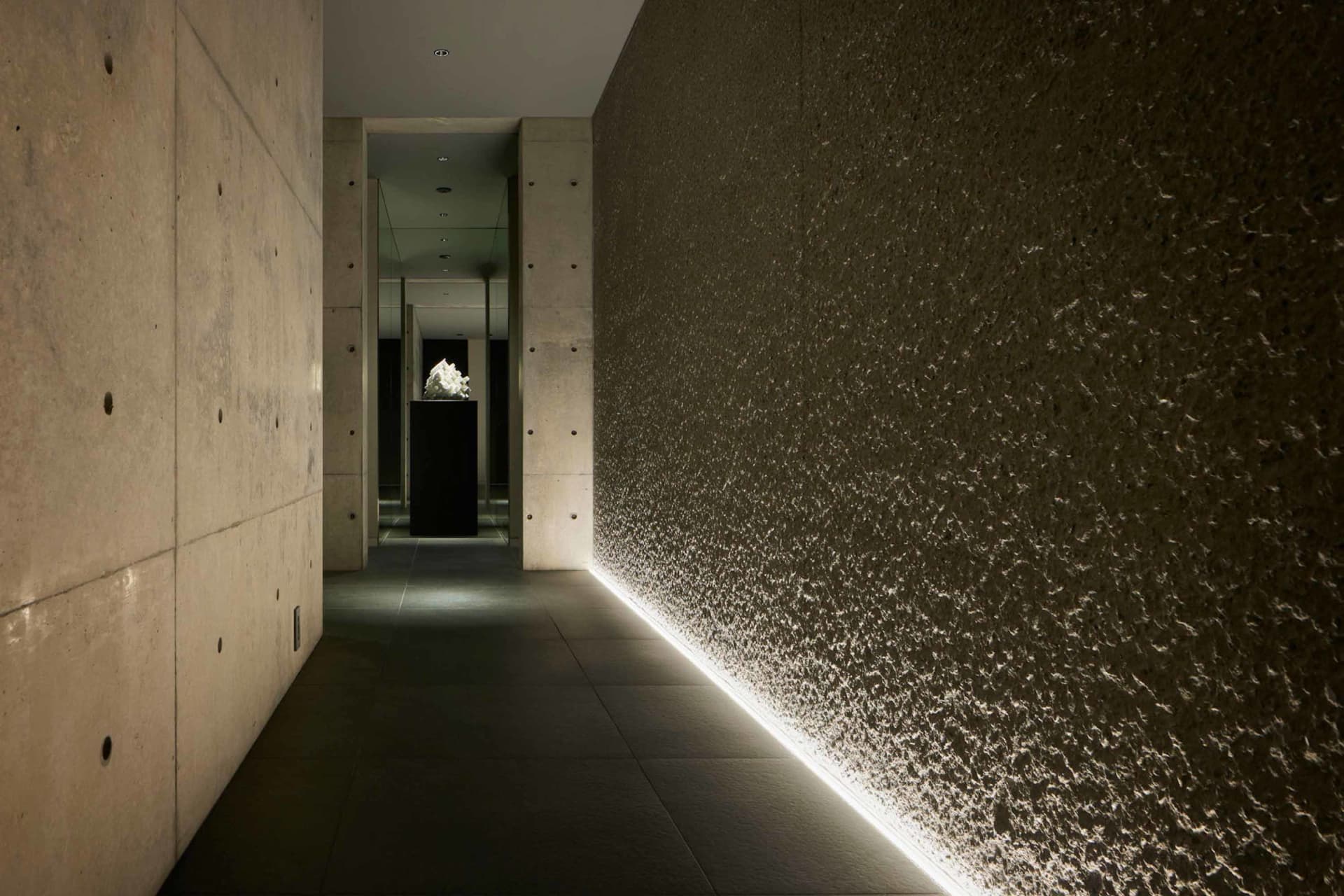 A modern interior space featuring textured concrete walls with lighting along the bottom edge, creating a minimalist and slee